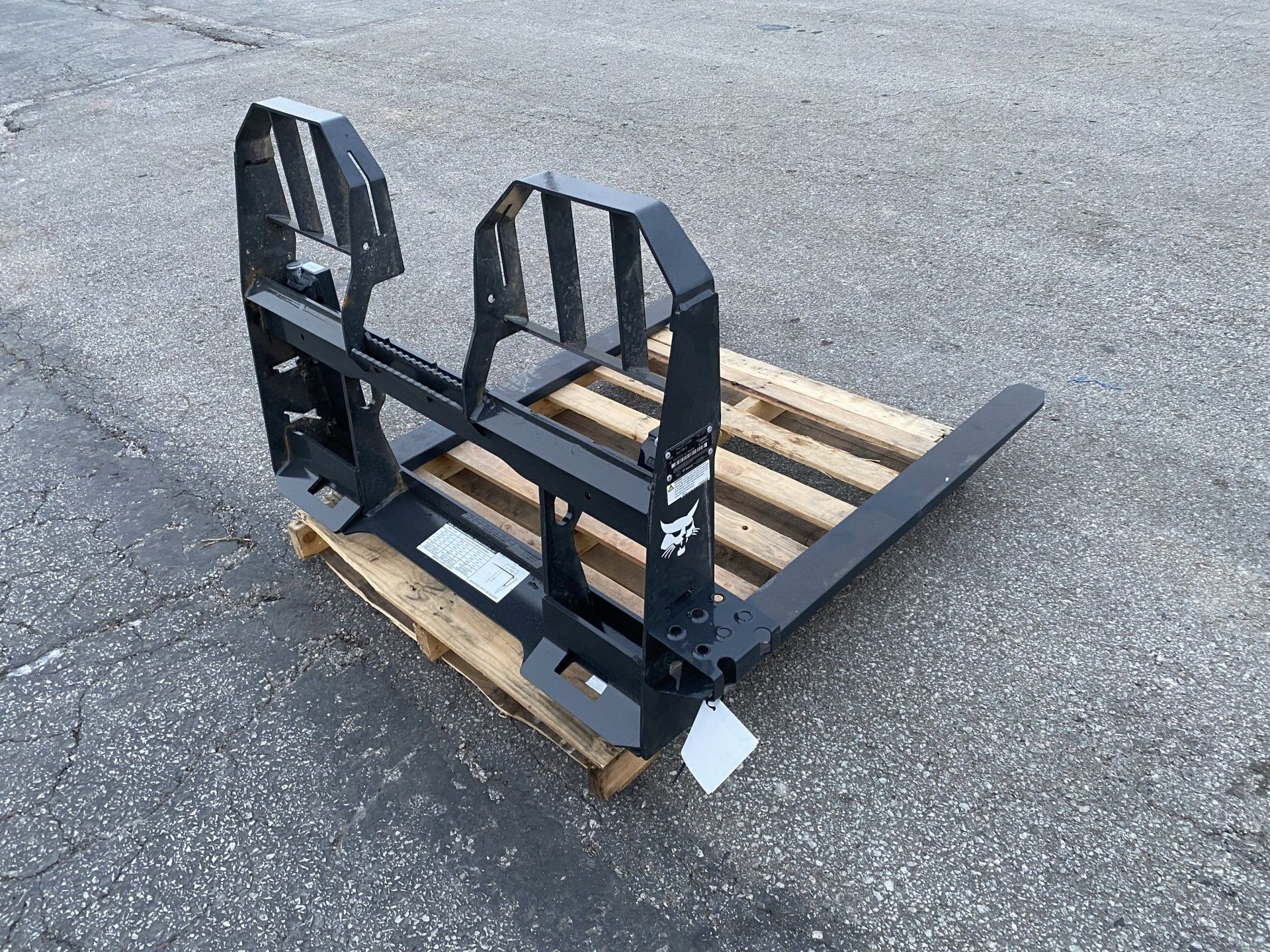 Black Bobcat pallet fork attachment on wooden pallet, outdoors.