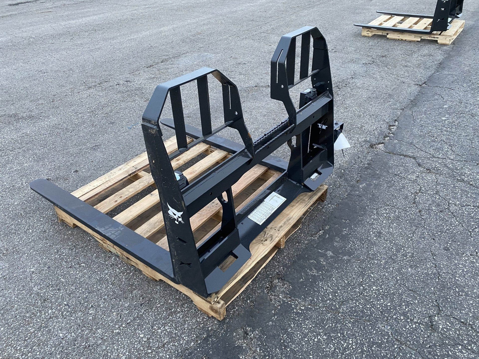Black forklift attachment resting on a wooden pallet outdoors on gray pavement.