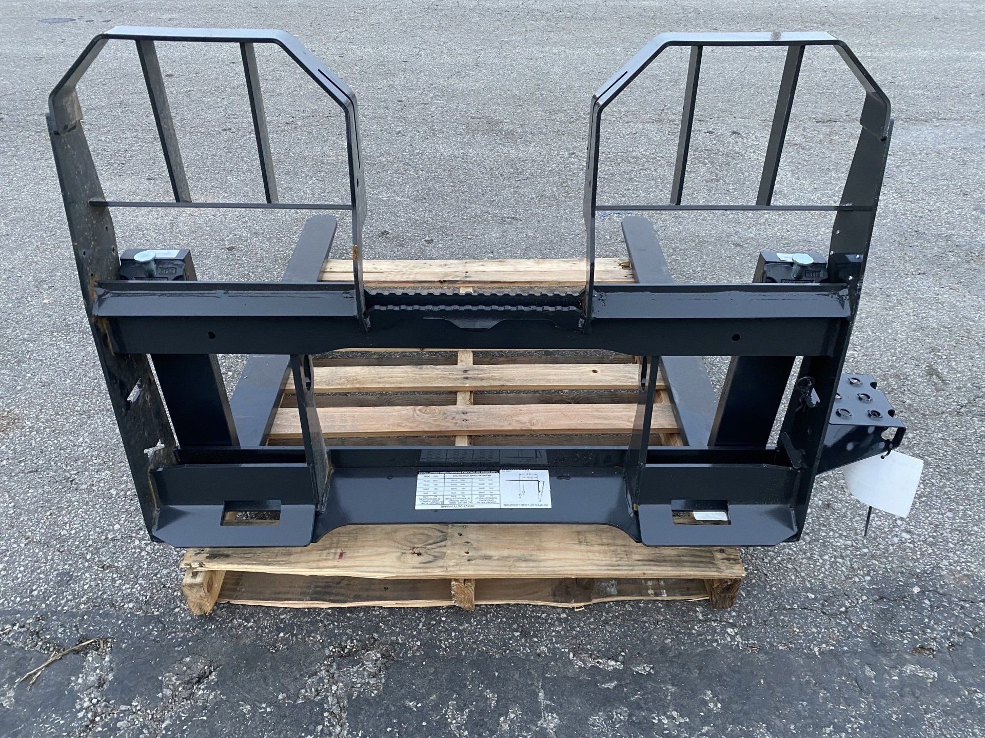 Black pallet fork attachment on a wooden pallet, outdoors.