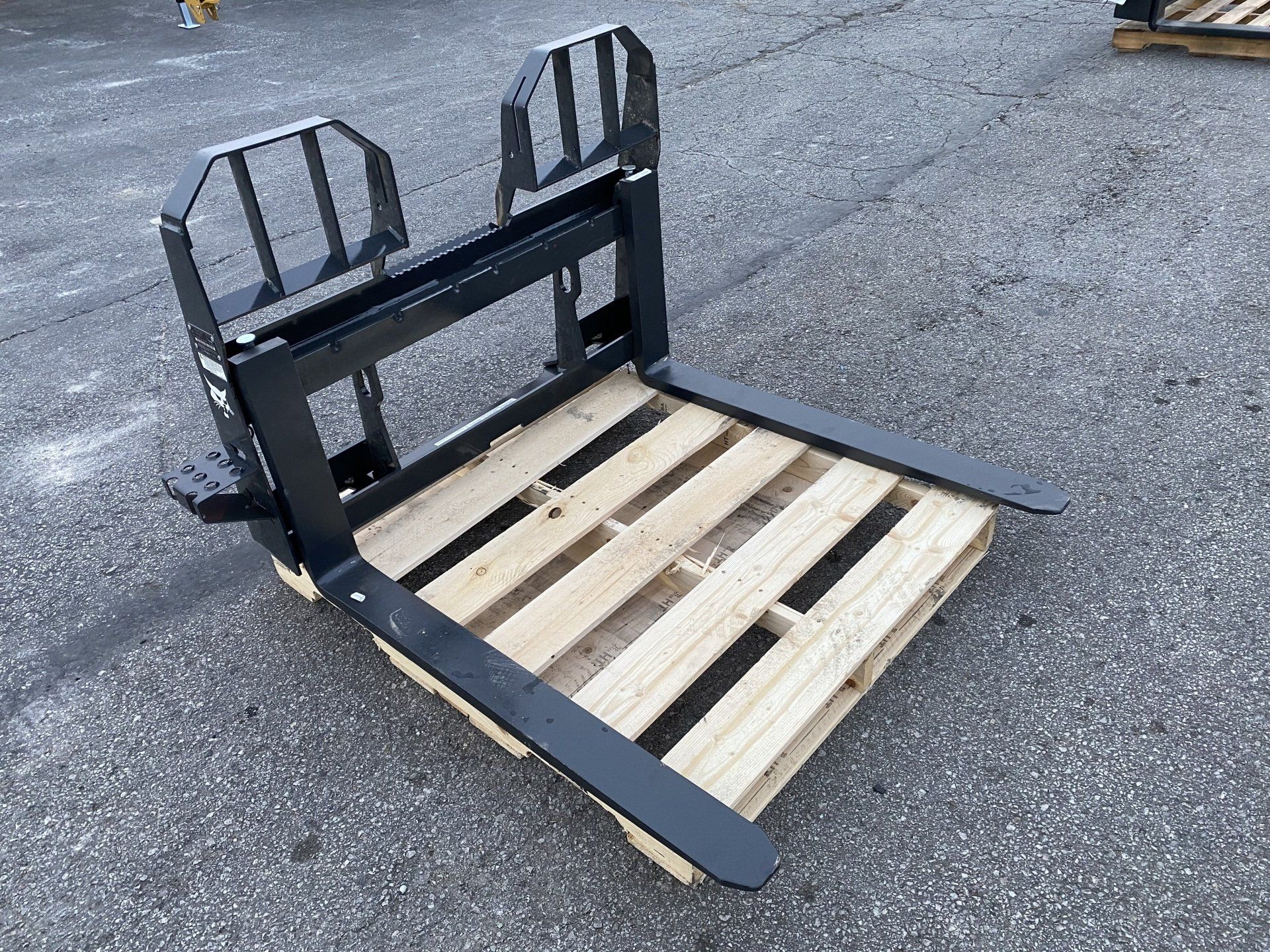 Black forklift attachment resting on a wooden pallet, outdoors.