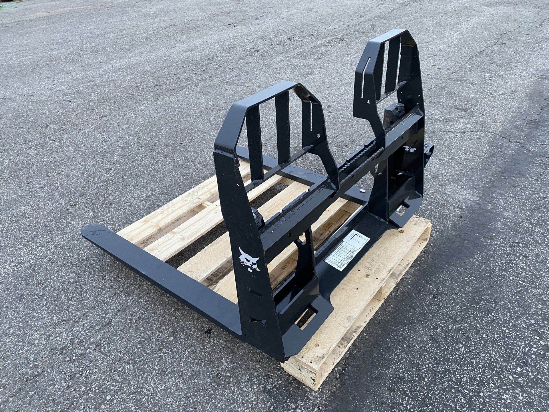 Black Bobcat pallet fork attachment on a wooden pallet, outdoors.