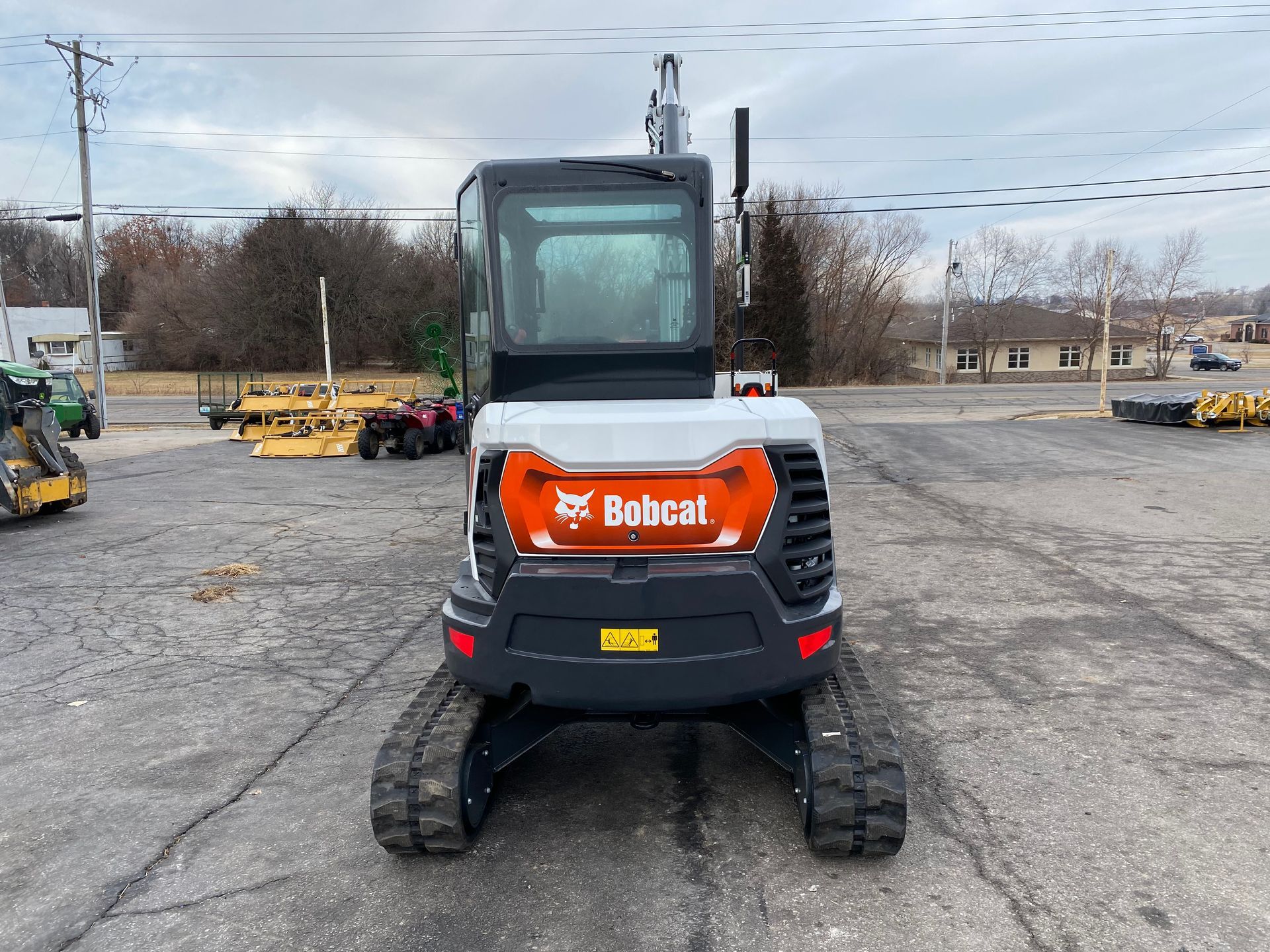 Bobcat excavator on tracks, parked on asphalt.  Orange, white, black, and gray machine.  Outdoor setting.