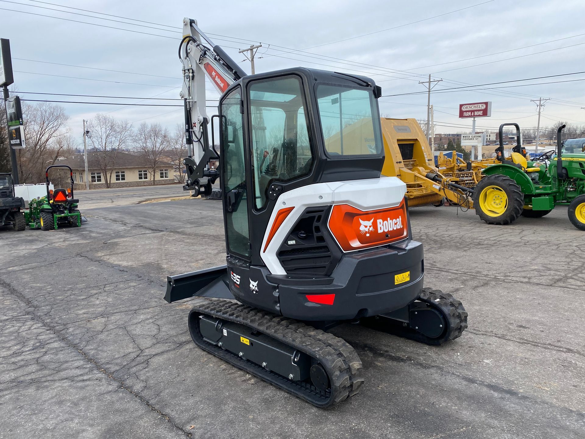 Bobcat compact excavator on pavement, cab with glass, orange and white logo, tracks.