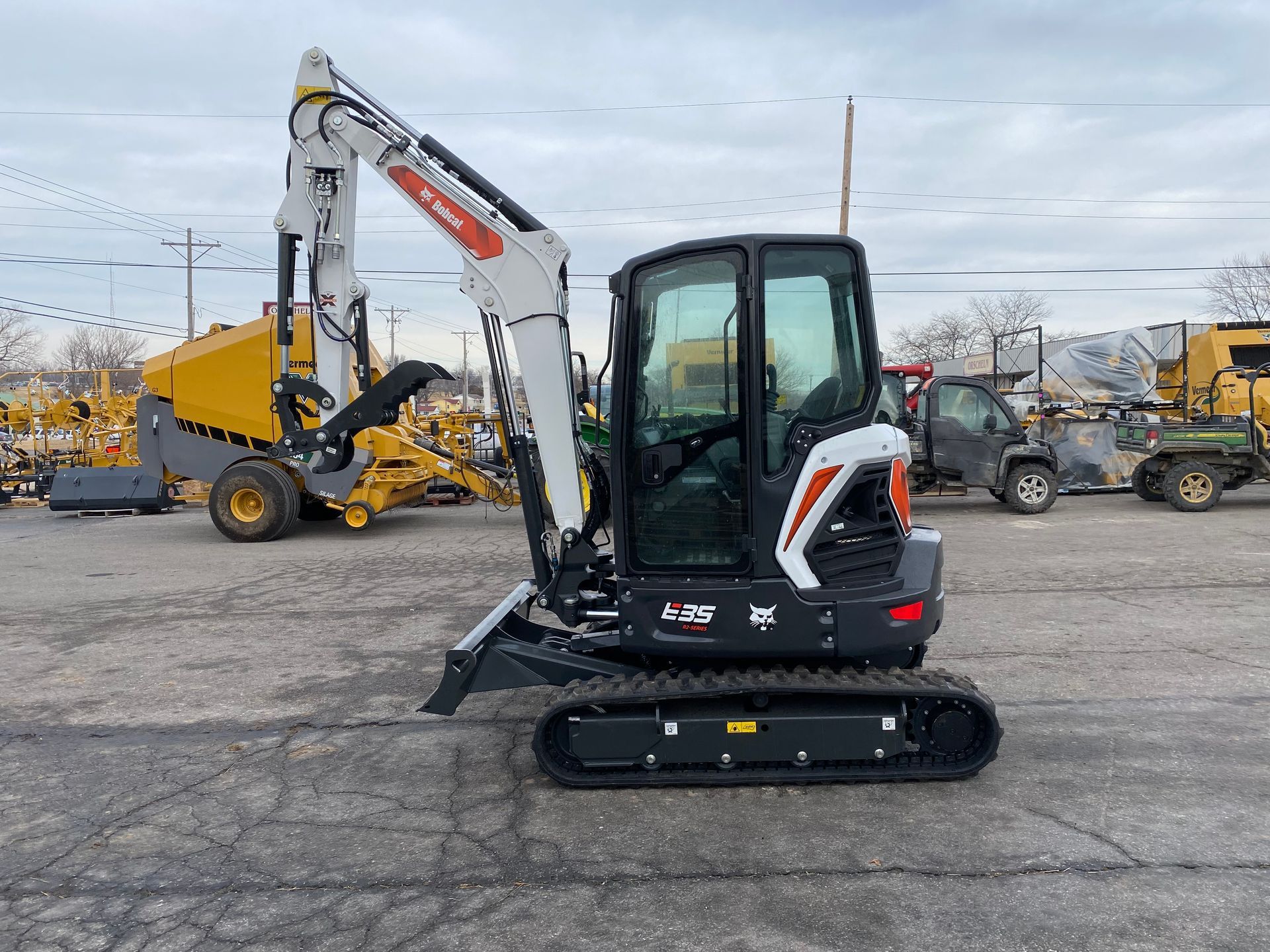 A white and black Bobcat excavator on a paved lot; other machinery in the background.