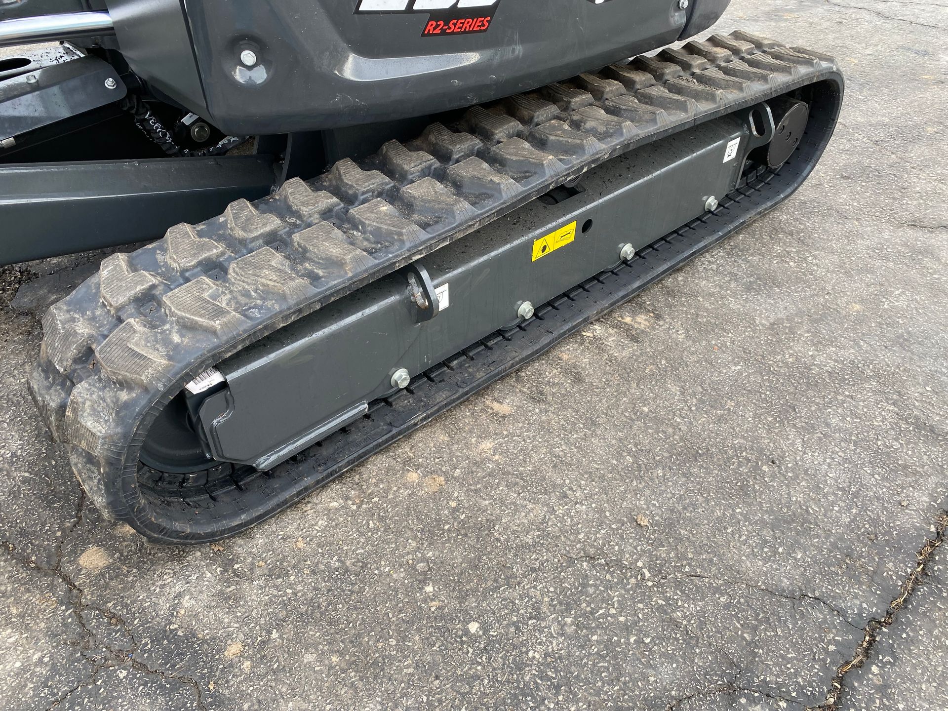 Close-up of a dark gray mini excavator track on a paved surface.