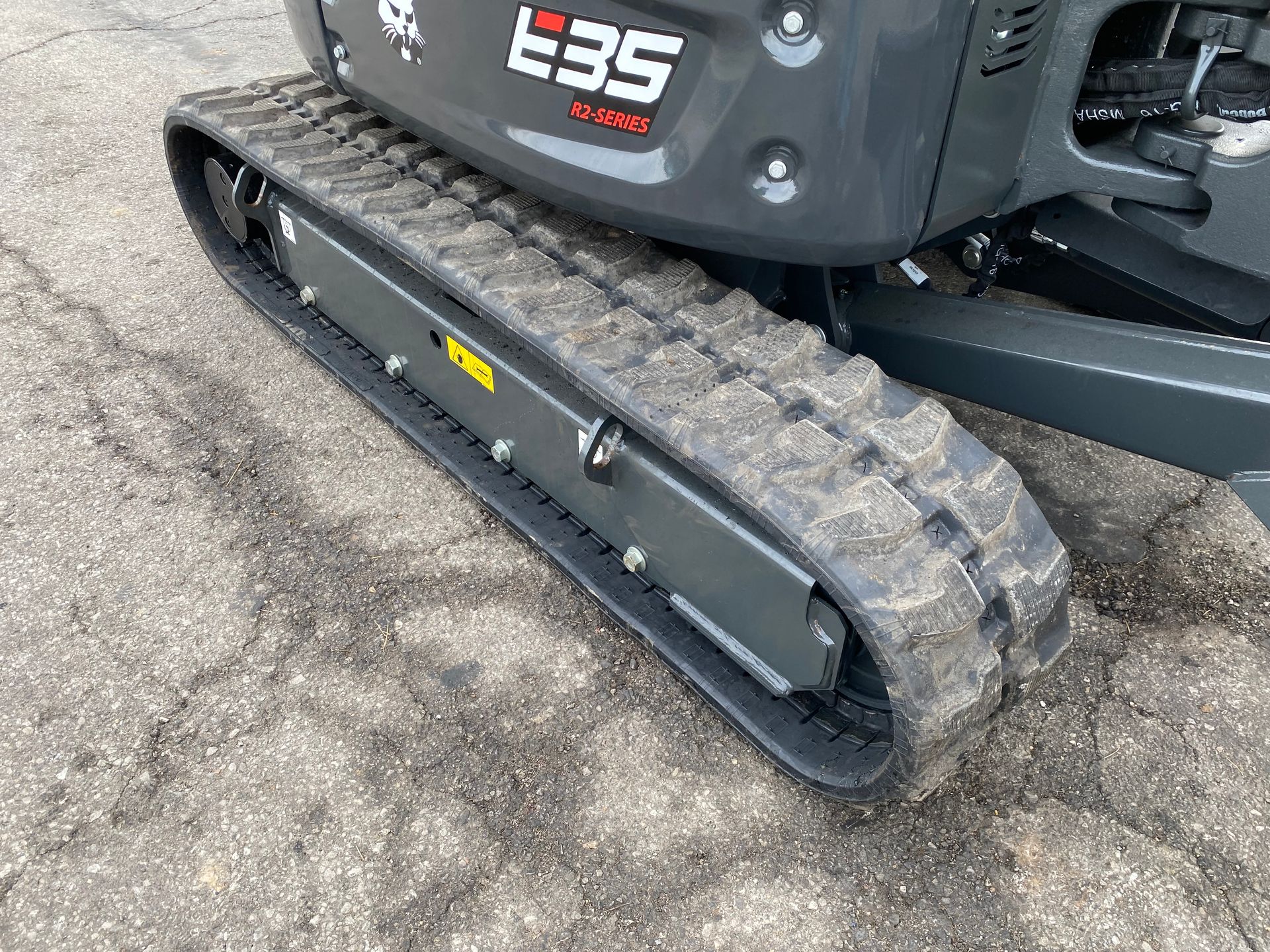 Close-up of a Bobcat E35 mini excavator track on asphalt. Gray and black.