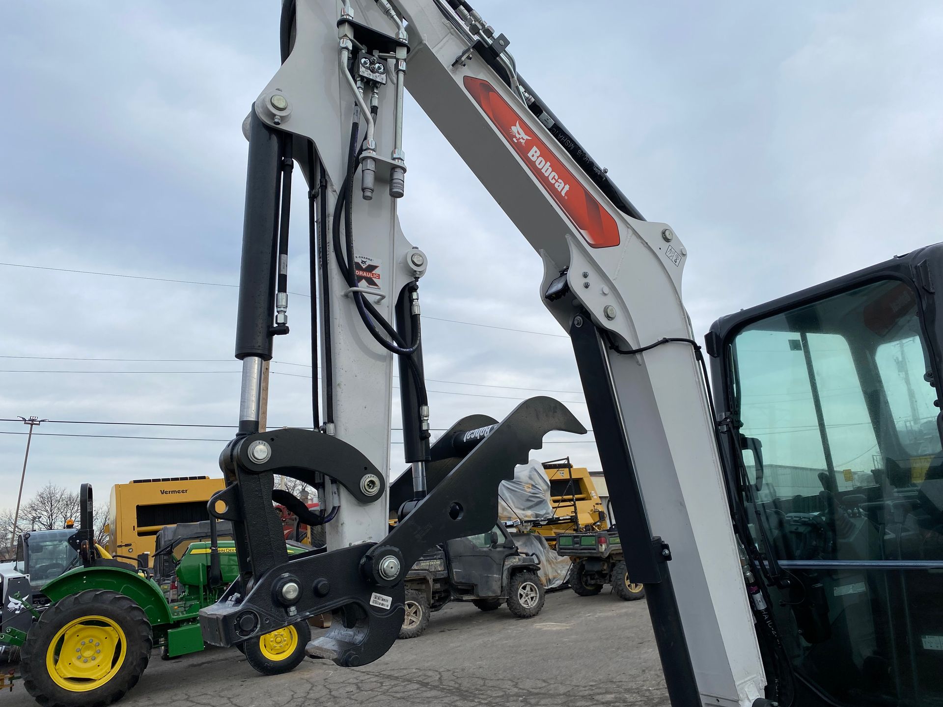 A Bobcat excavator arm with grapple attachment, outdoors, overcast day.