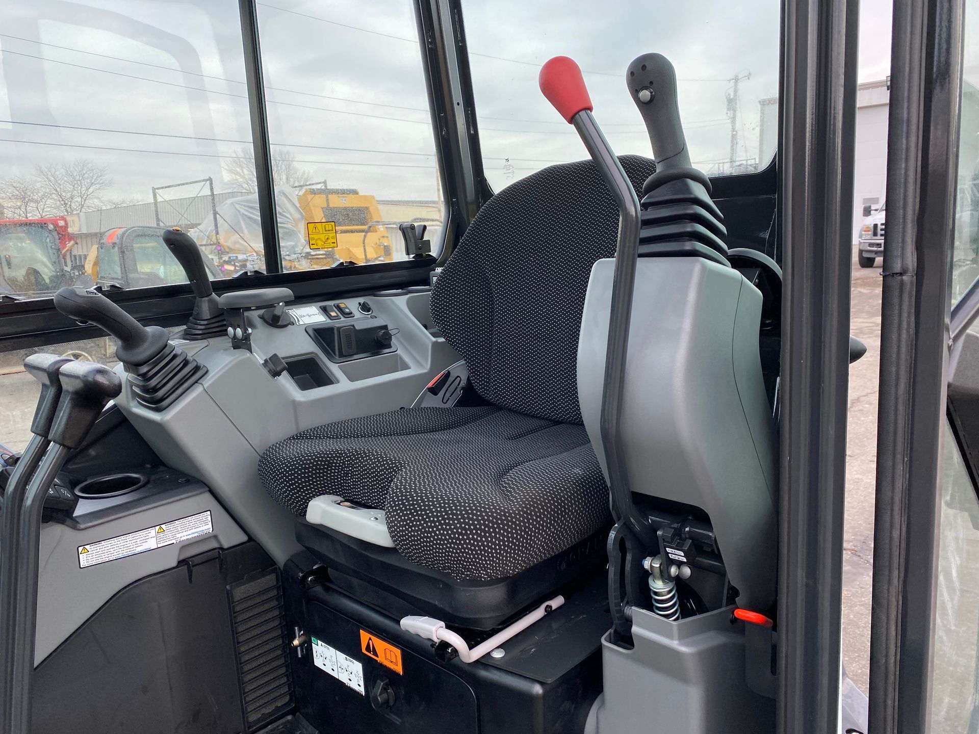 Interior of an excavator cab with seat, controls, and levers. Gray and black.