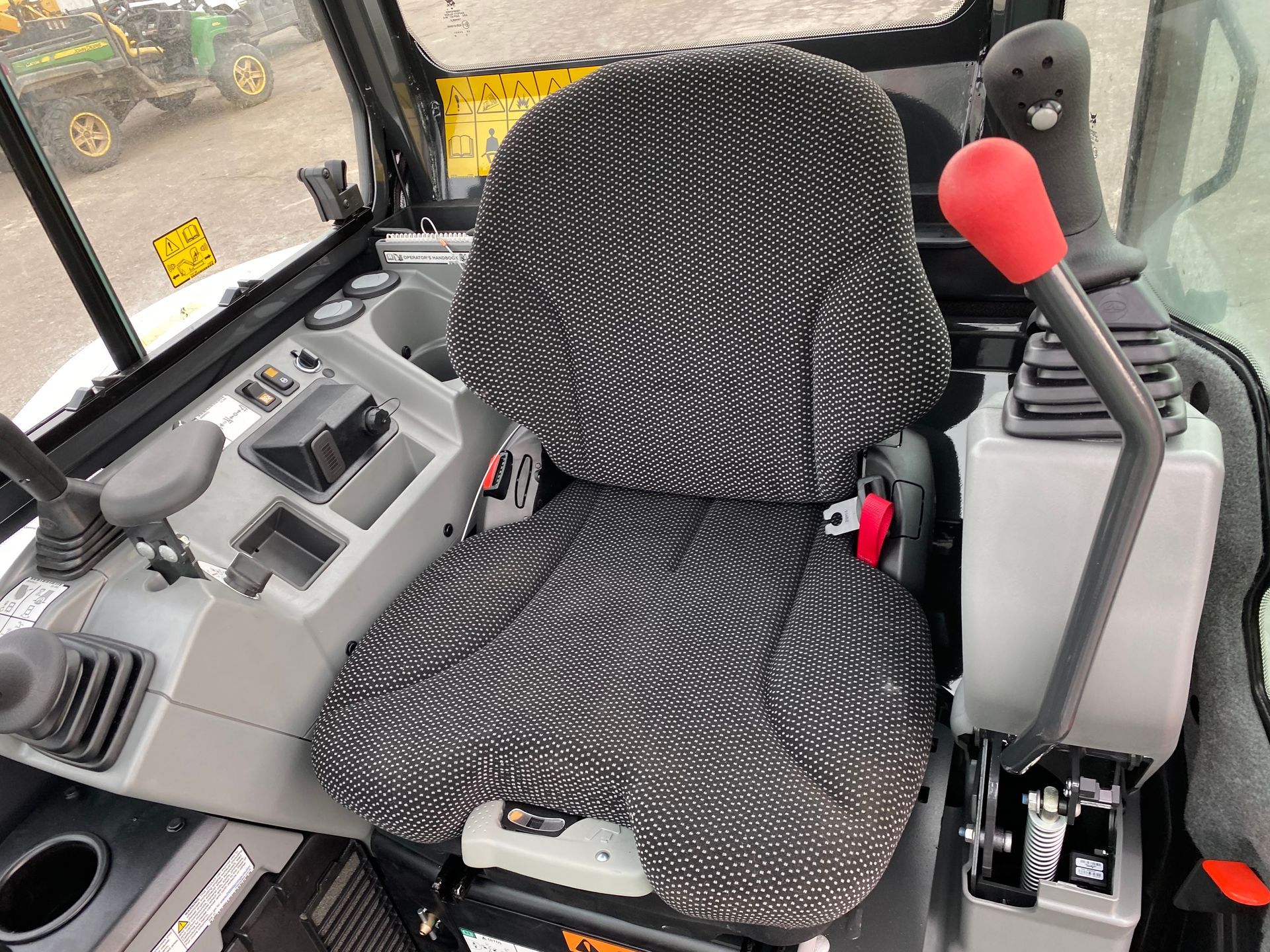 Interior view of an excavator cab with a patterned seat, control levers, and gauges.