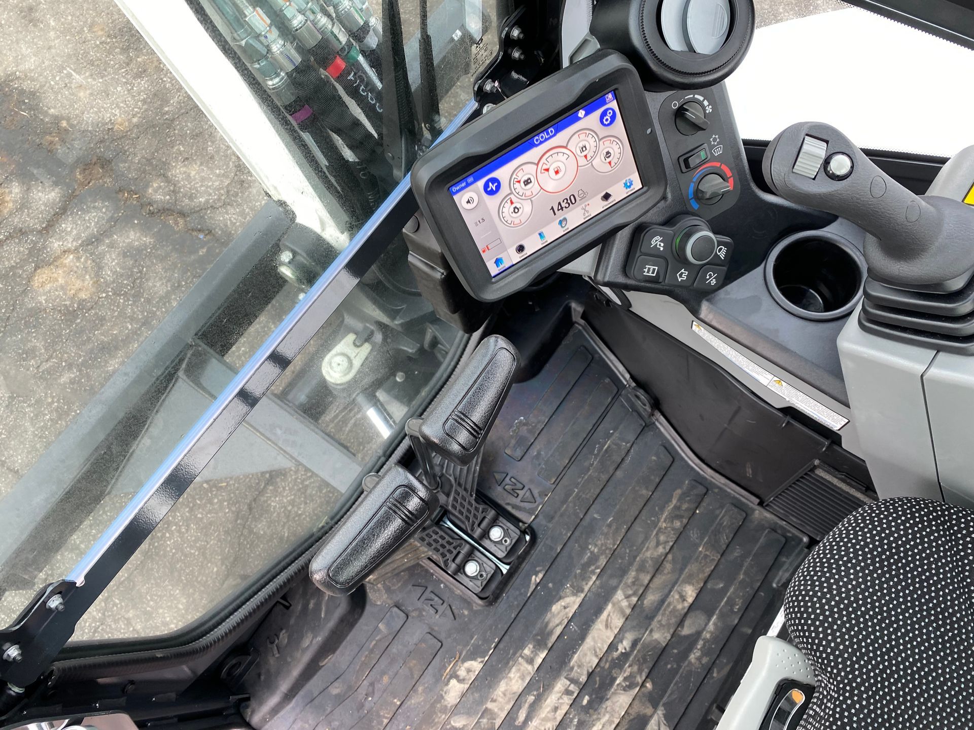 Interior of excavator cabin with display screen, controls, and foot pedals.