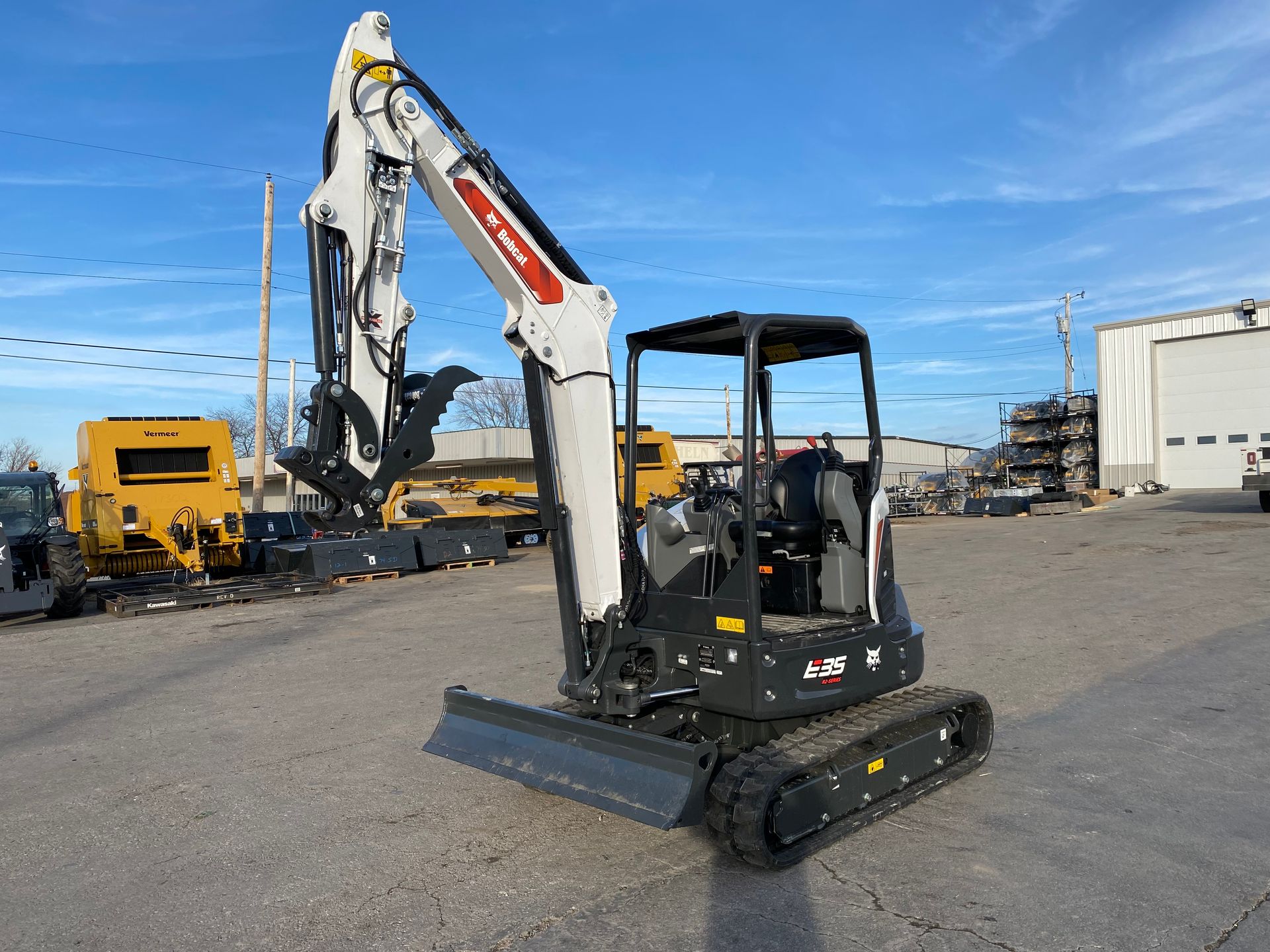 Bobcat compact excavator with arm raised, on a concrete lot, against a blue sky.