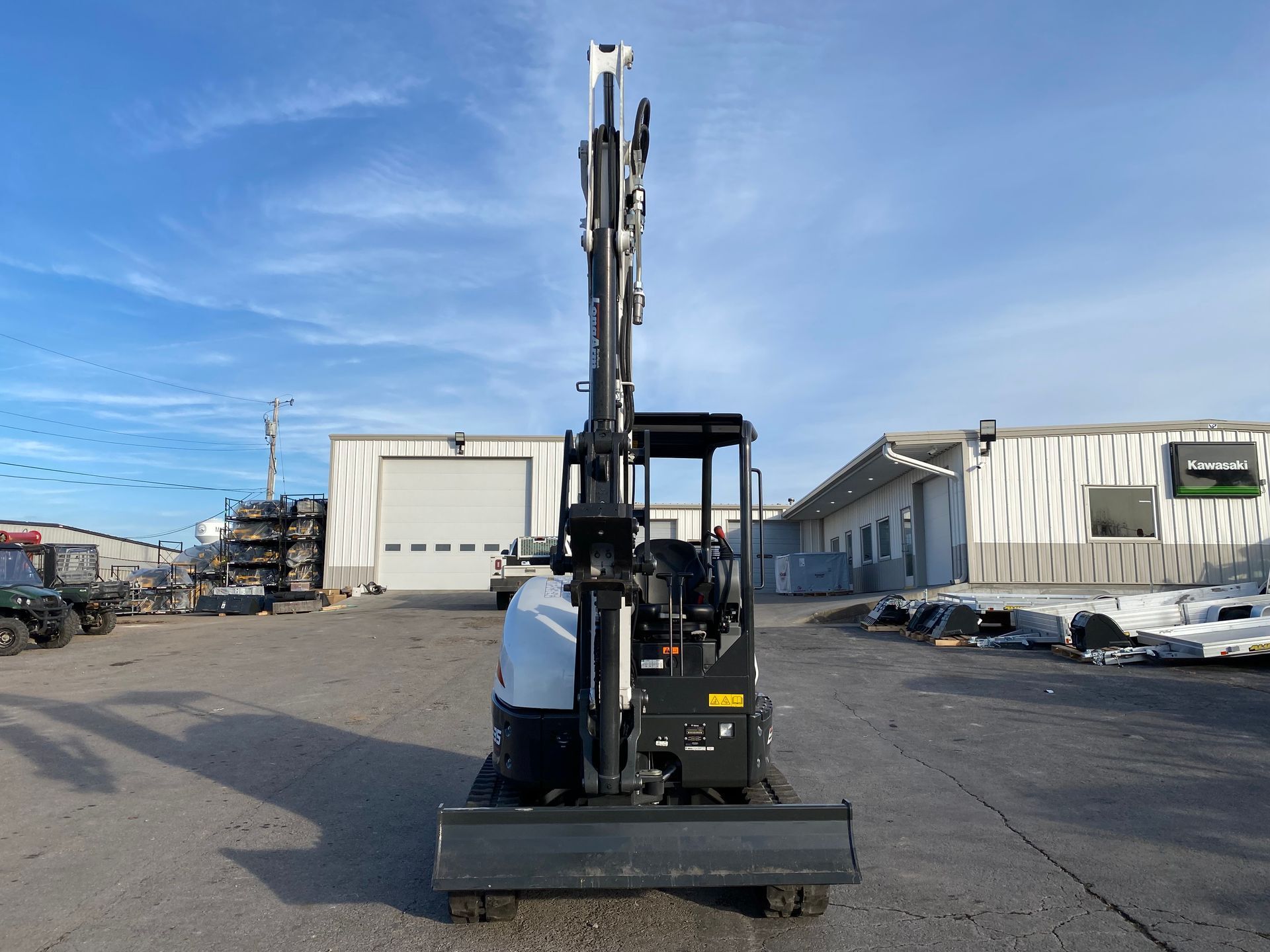 Bobcat excavator with raised arm in front of buildings on a sunny day.