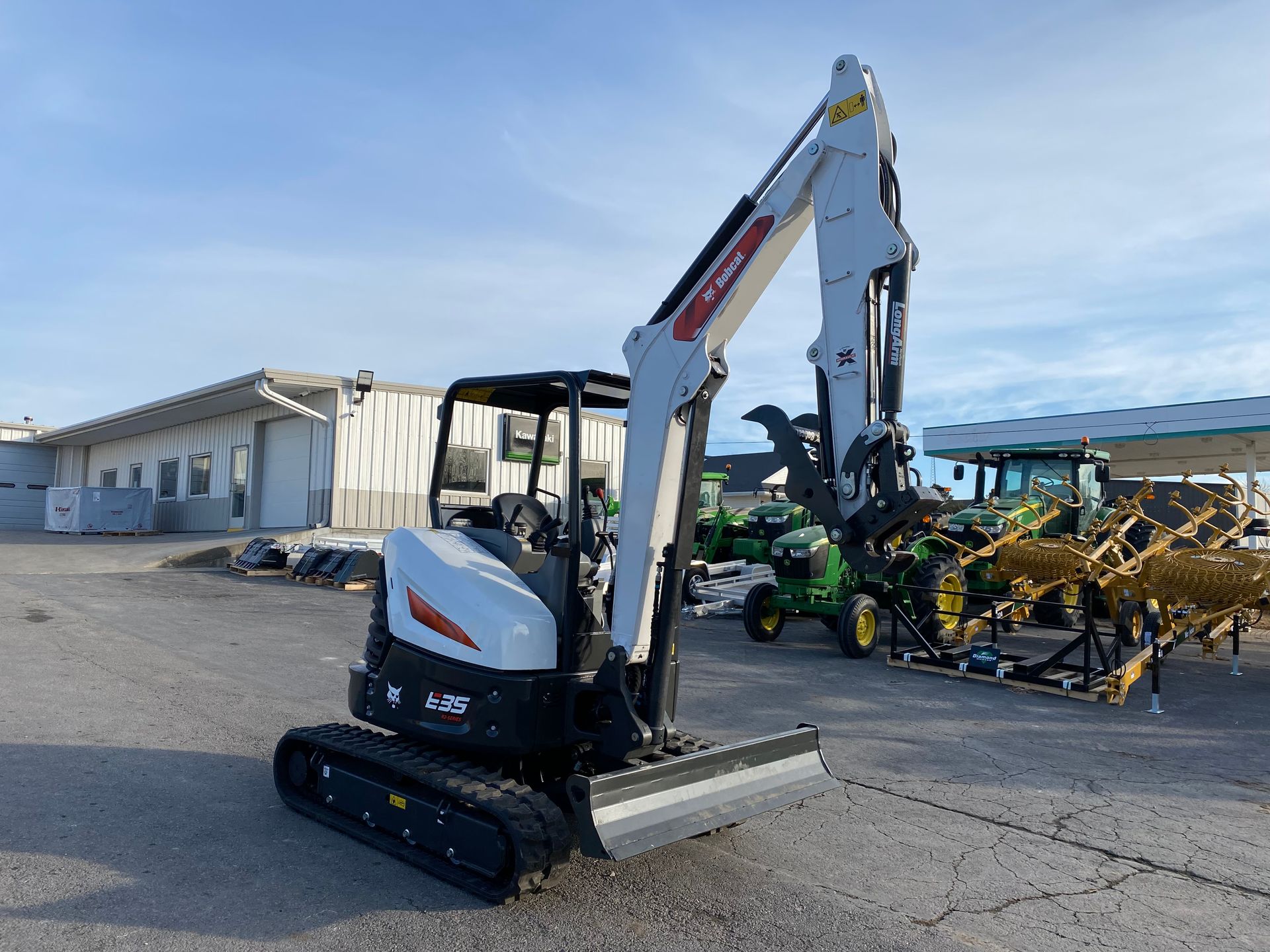 White Bobcat excavator on tracks parked outside, near a building and farm equipment.