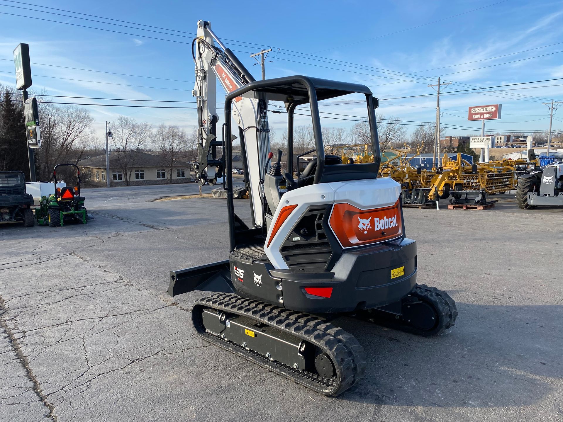 Bobcat E16 mini excavator on tracks outdoors. White, black, and orange. Sunny day.