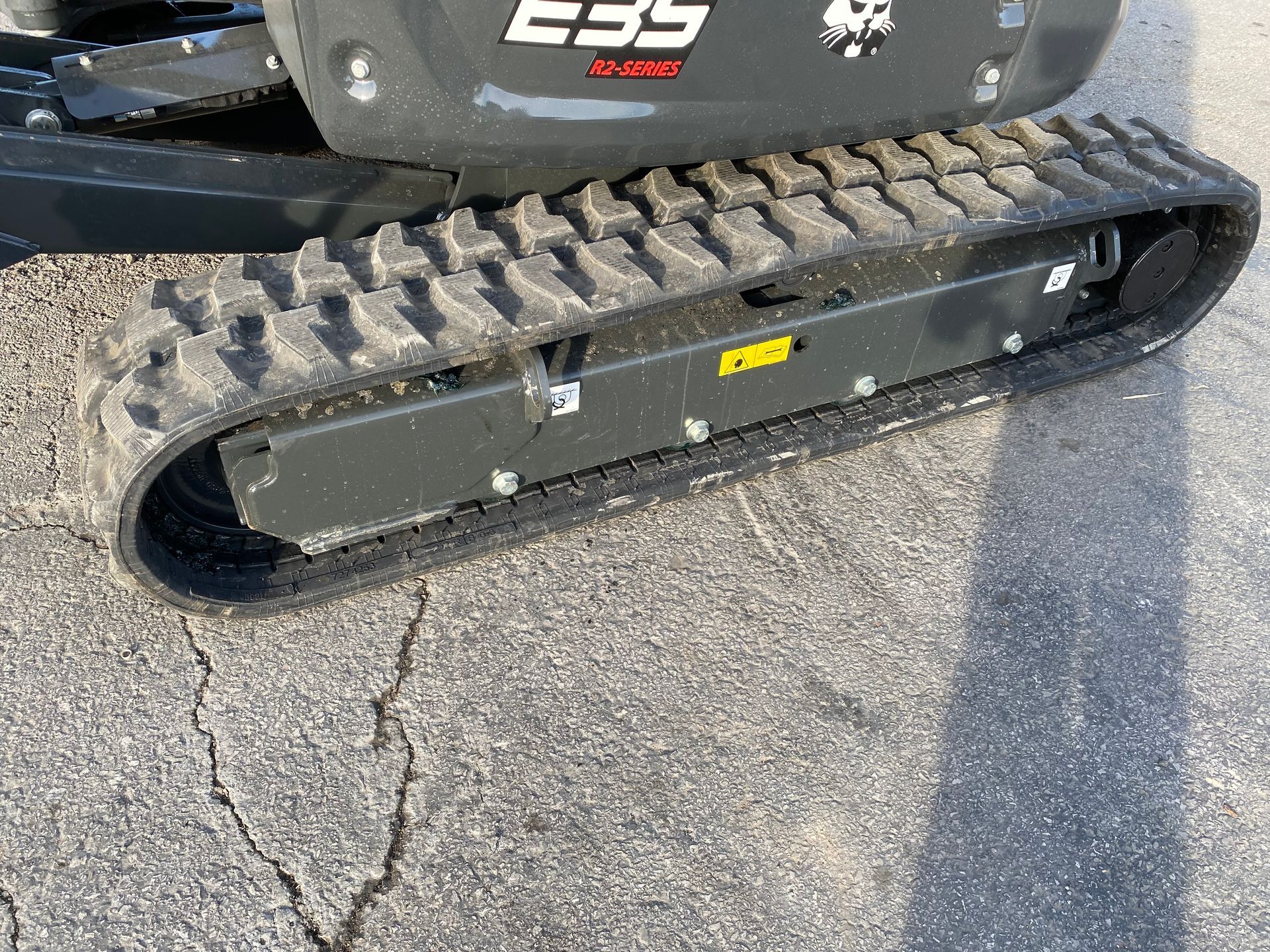 Black Bobcat E35 excavator track on cracked pavement.