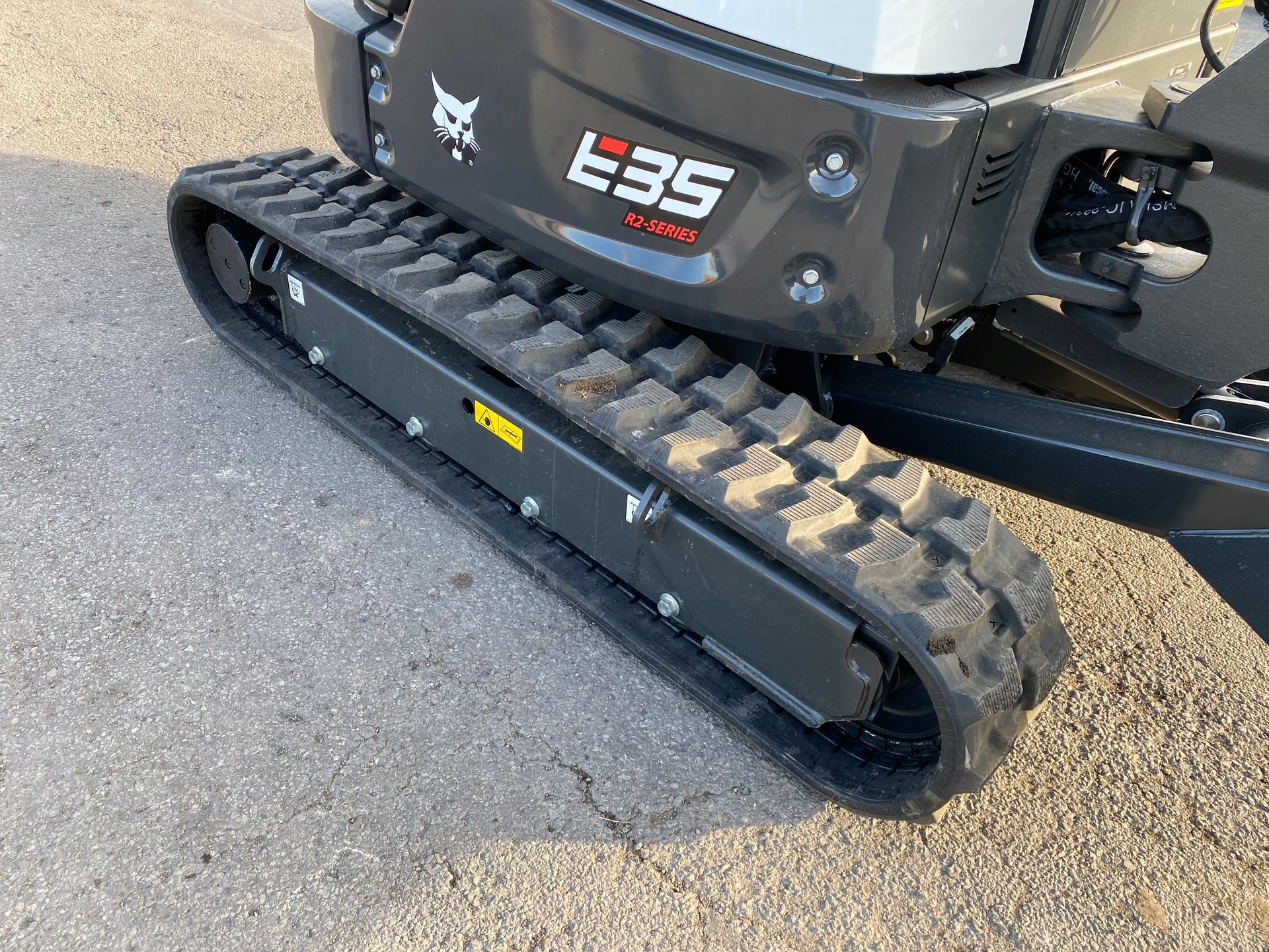 A close-up of a Bobcat E35 mini excavator track. The track is black rubber and rests on pavement.