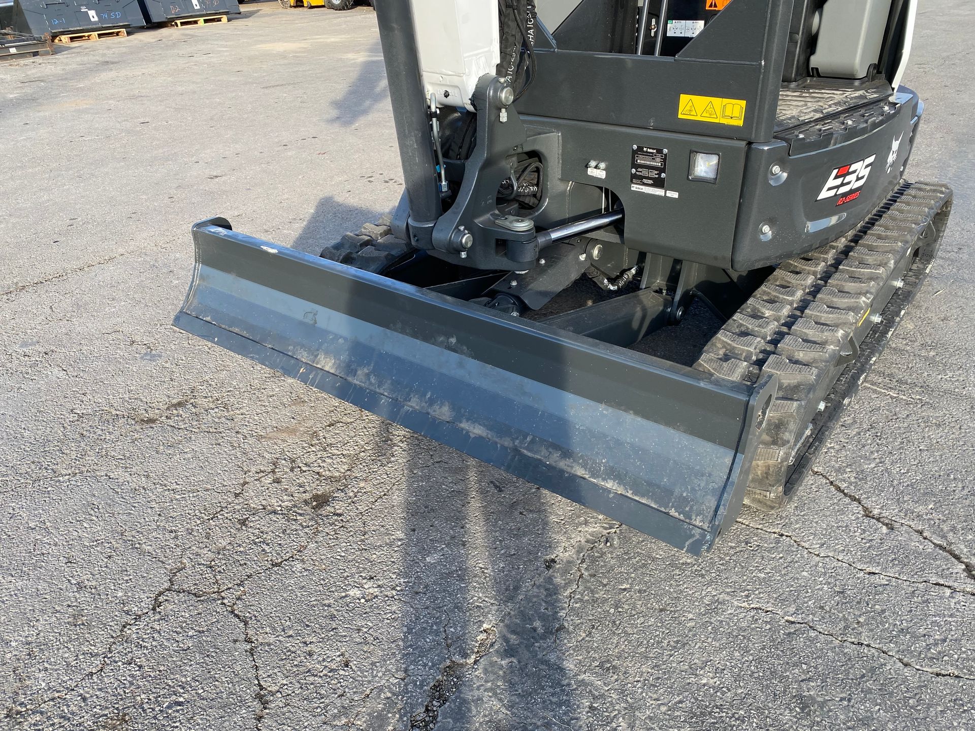 Small, gray Bobcat E35 mini excavator with a front blade on a cracked asphalt surface.