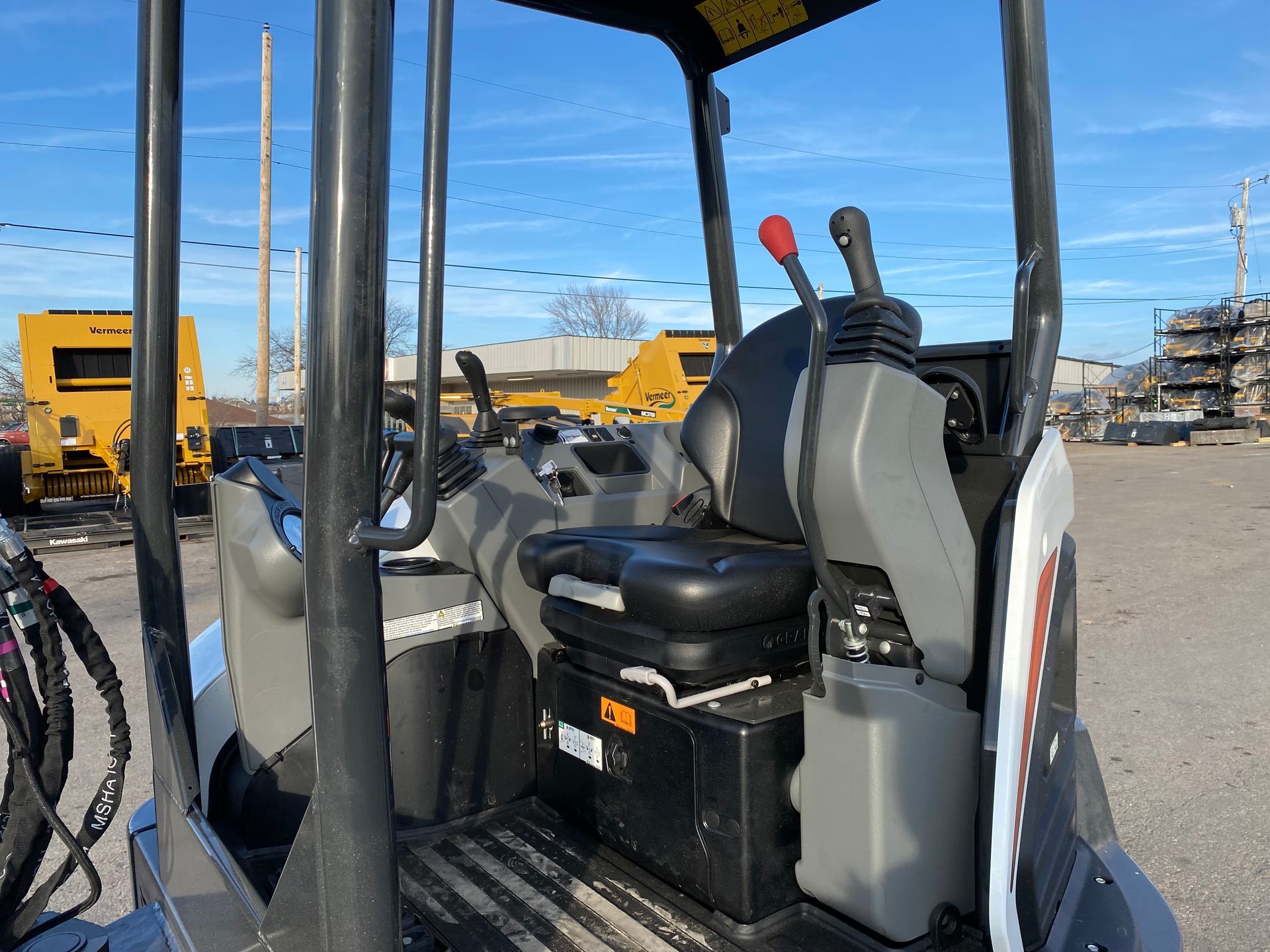 Interior of a Bobcat mini excavator: seat, control levers, safety bars, and other machinery visible.