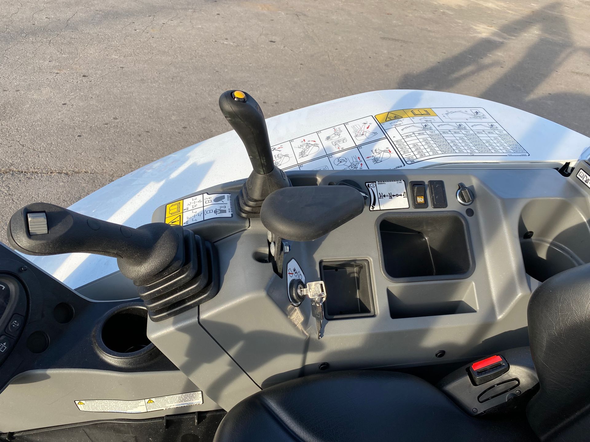 Control panel of a small, white construction vehicle. Black joysticks, keys, and switches are visible.
