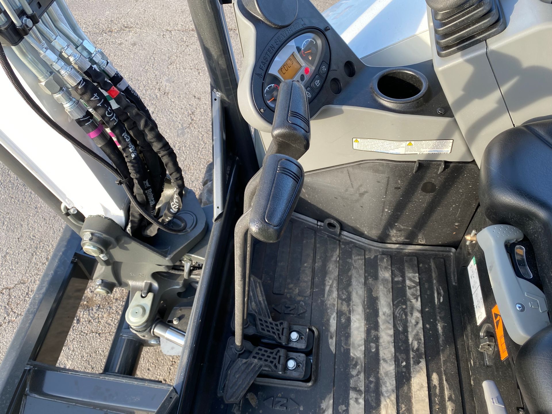 Interior of an excavator cab with control levers, pedals, and gauges. Black and gray, machinery.