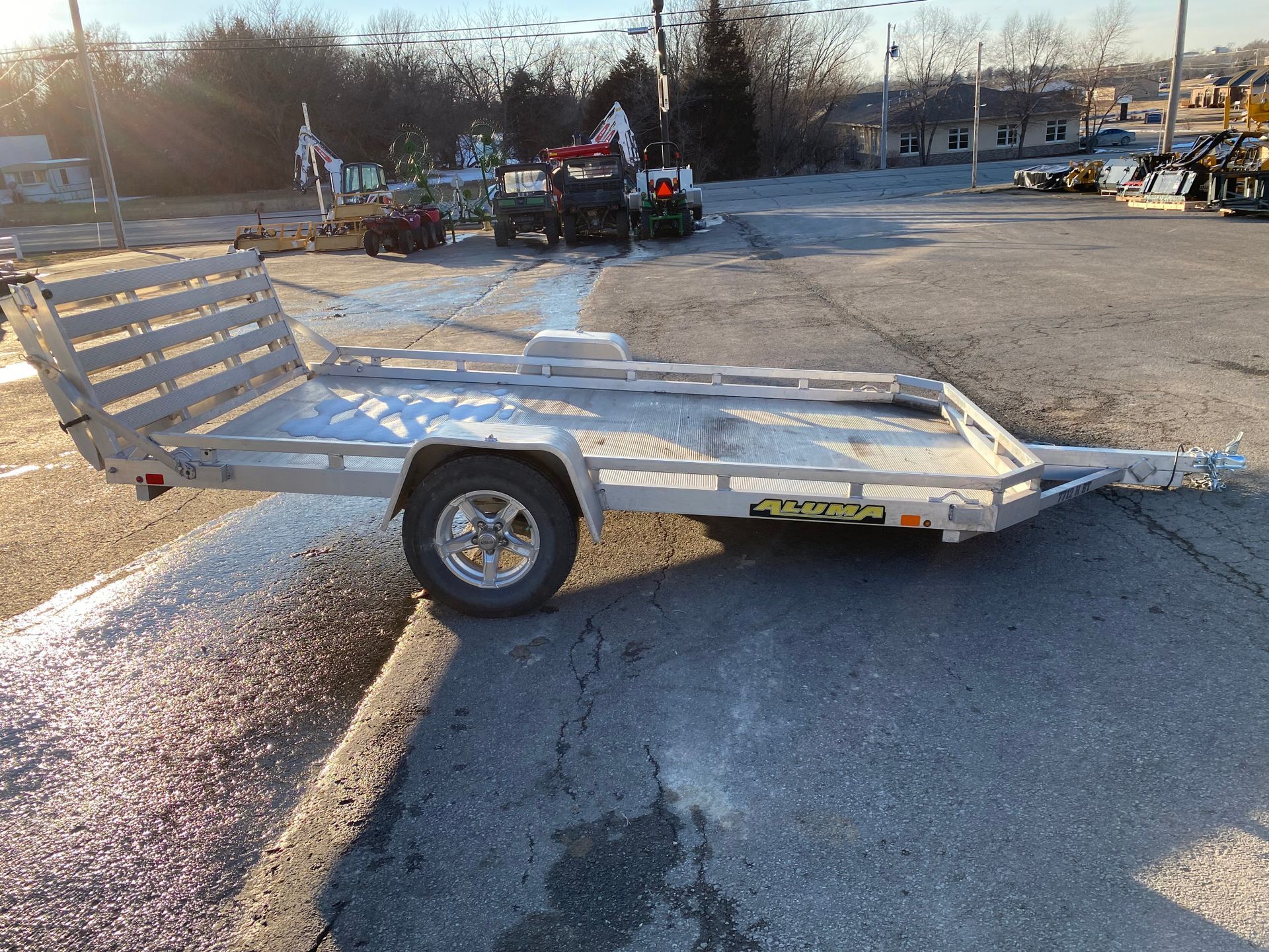 Silver utility trailer on asphalt in front of buildings.