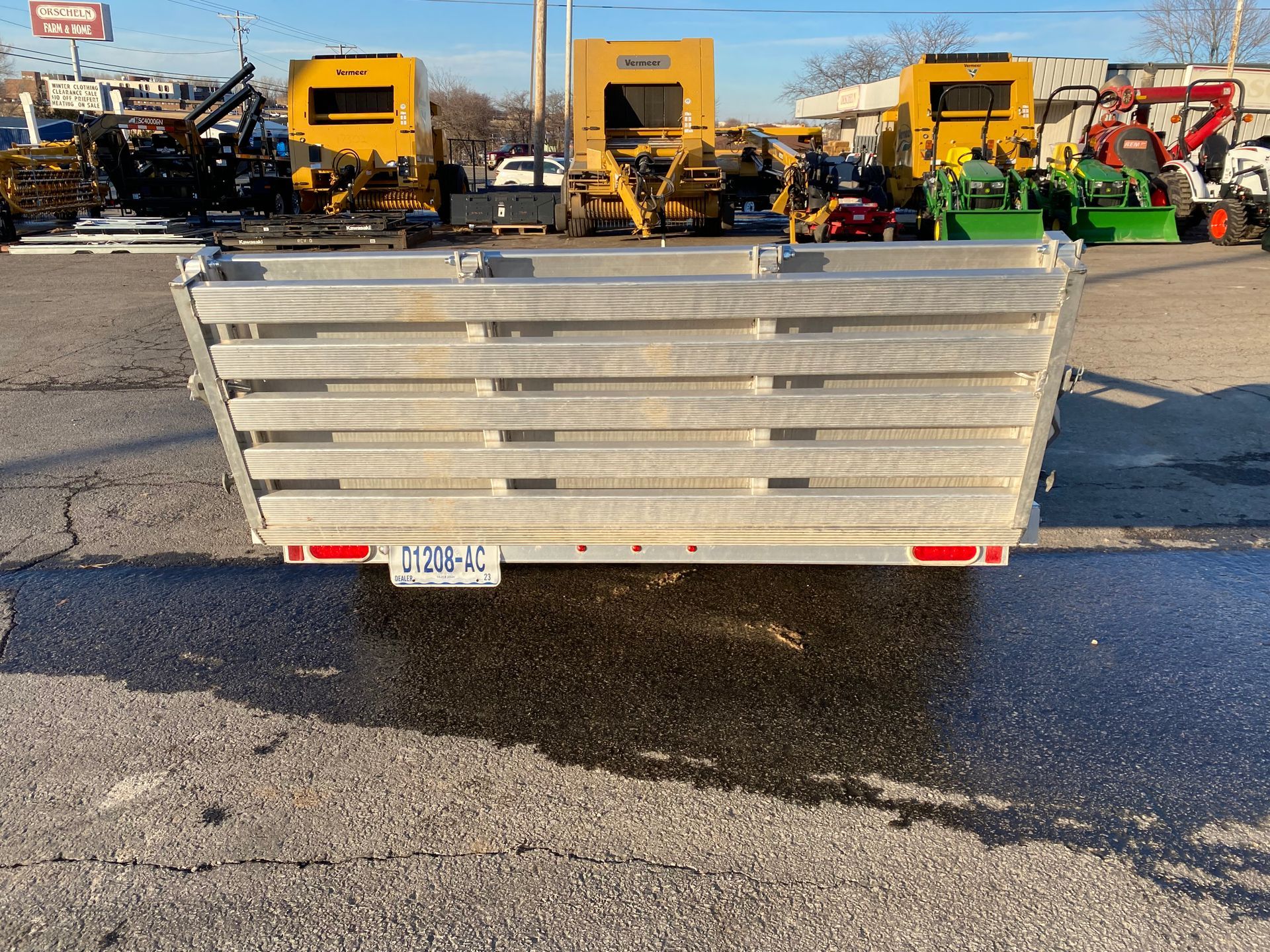Gray dump trailer with a license plate, parked on asphalt; heavy equipment in background.