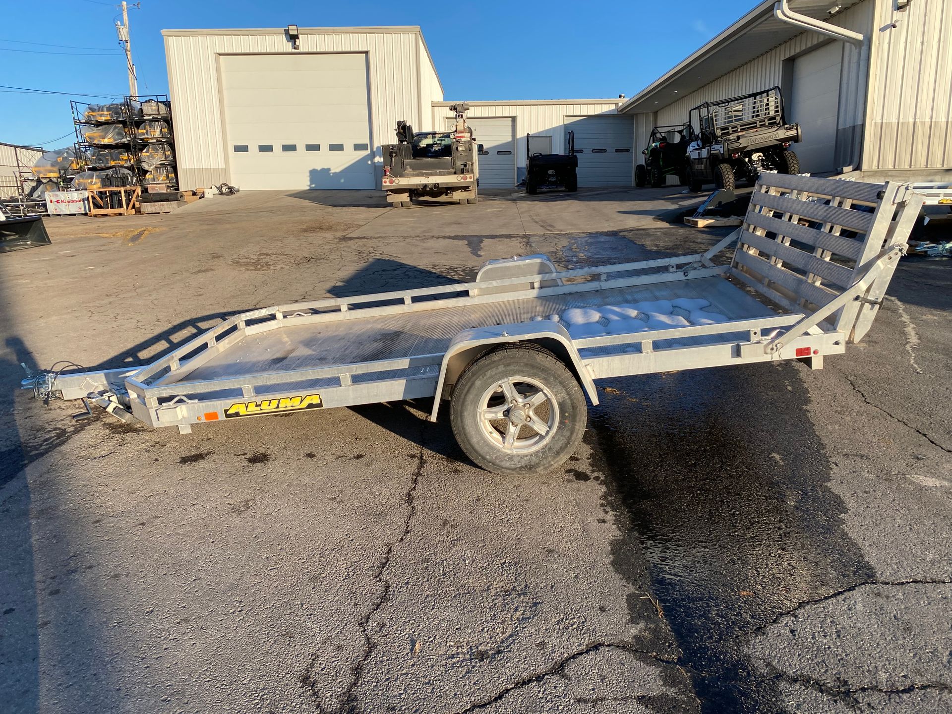 Silver utility trailer parked in front of a building with a closed garage door.
