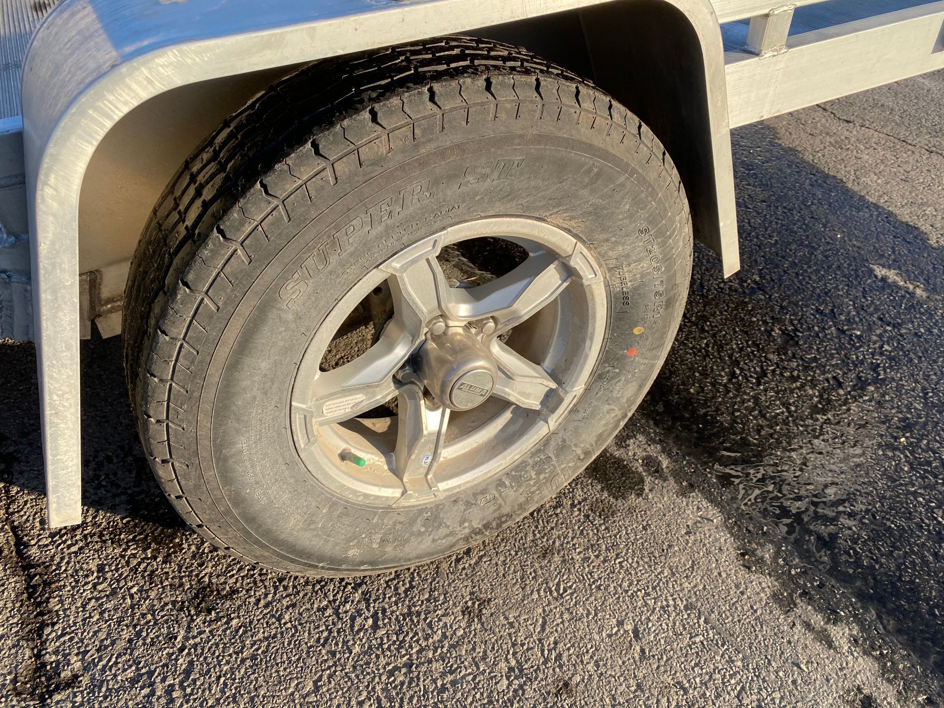 Trailer tire, gray with silver rim, parked on asphalt.