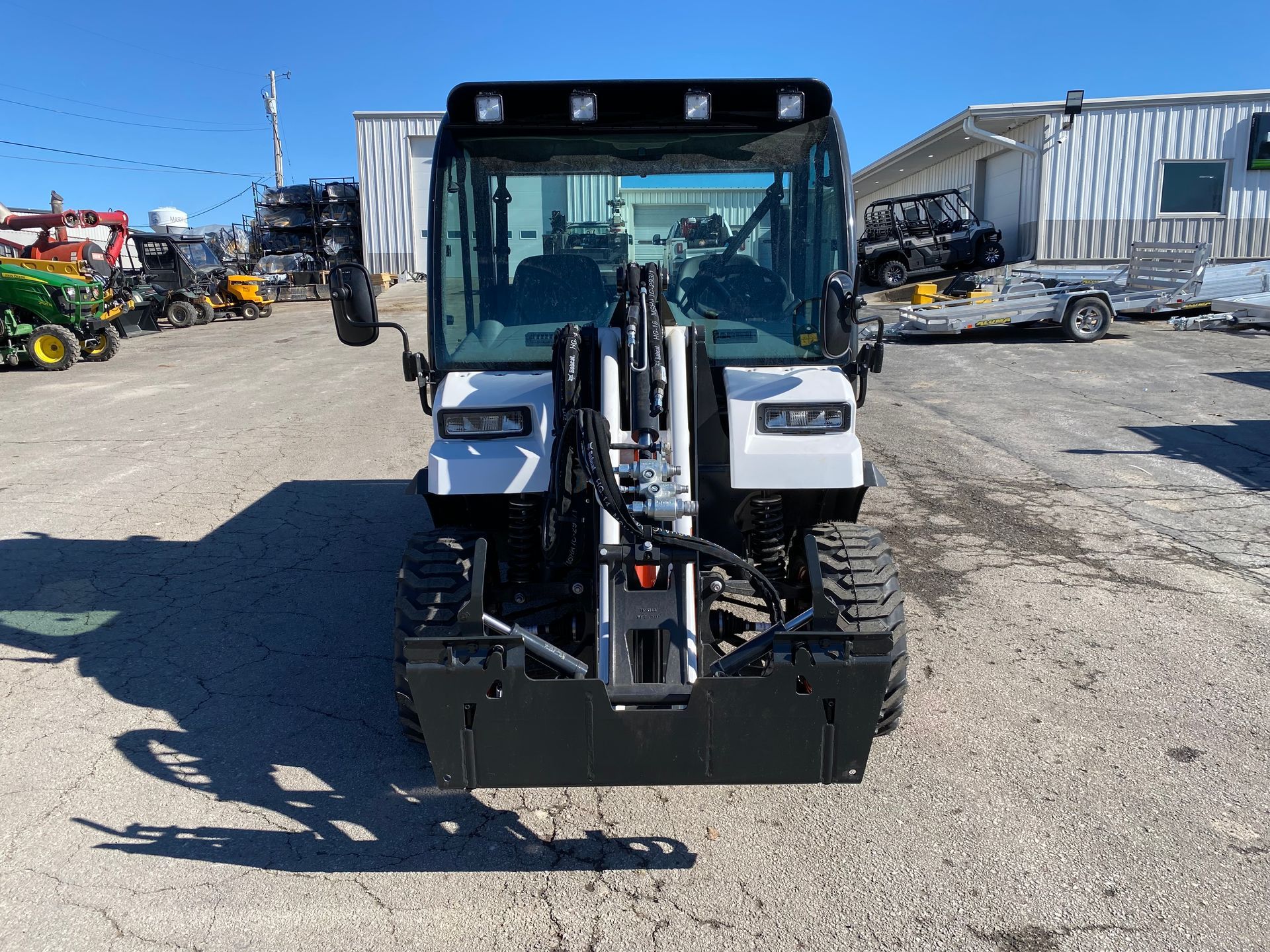 White and black compact tractor with a glass-enclosed cab, parked on a paved lot.