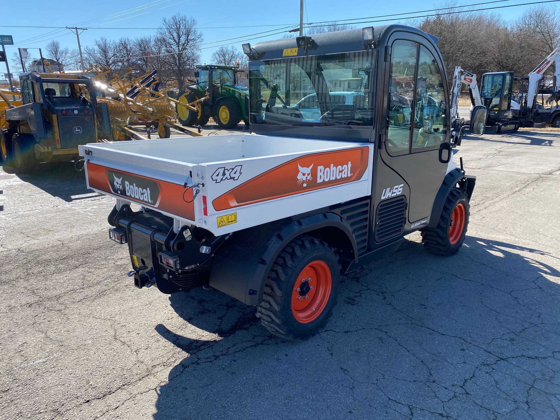 Bobcat utility vehicle with white bed, orange wheels, and enclosed cab, parked outside.