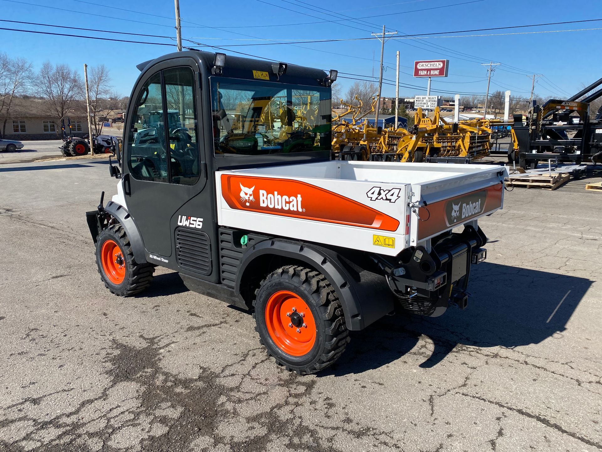 Bobcat utility vehicle with white cargo bed, orange wheels, and enclosed cab. Parked outside.