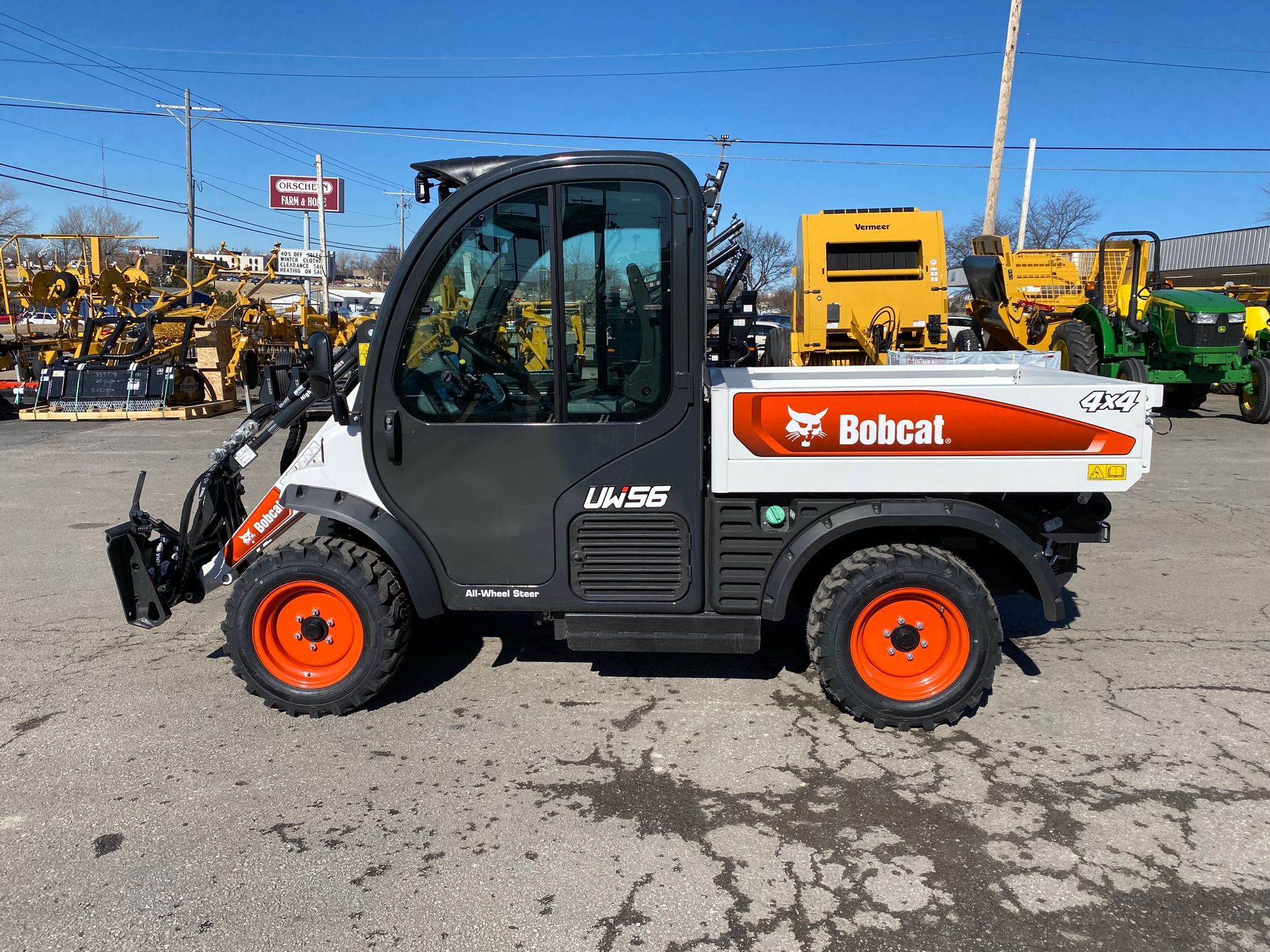 Bobcat utility vehicle with orange wheels, in a lot with other machinery.
