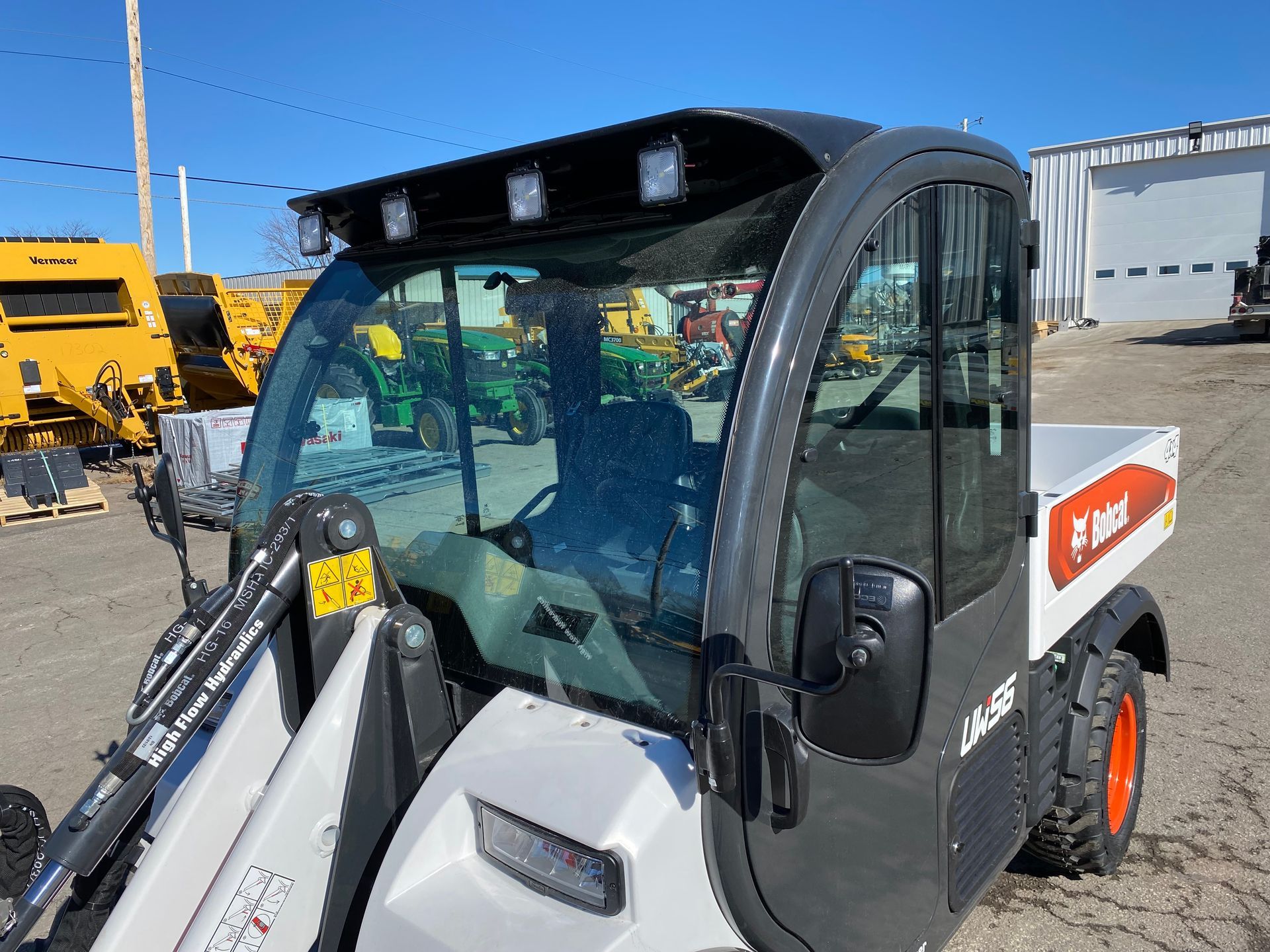 Bobcat utility vehicle with a cab and lights. Outdoor setting, bright blue sky.