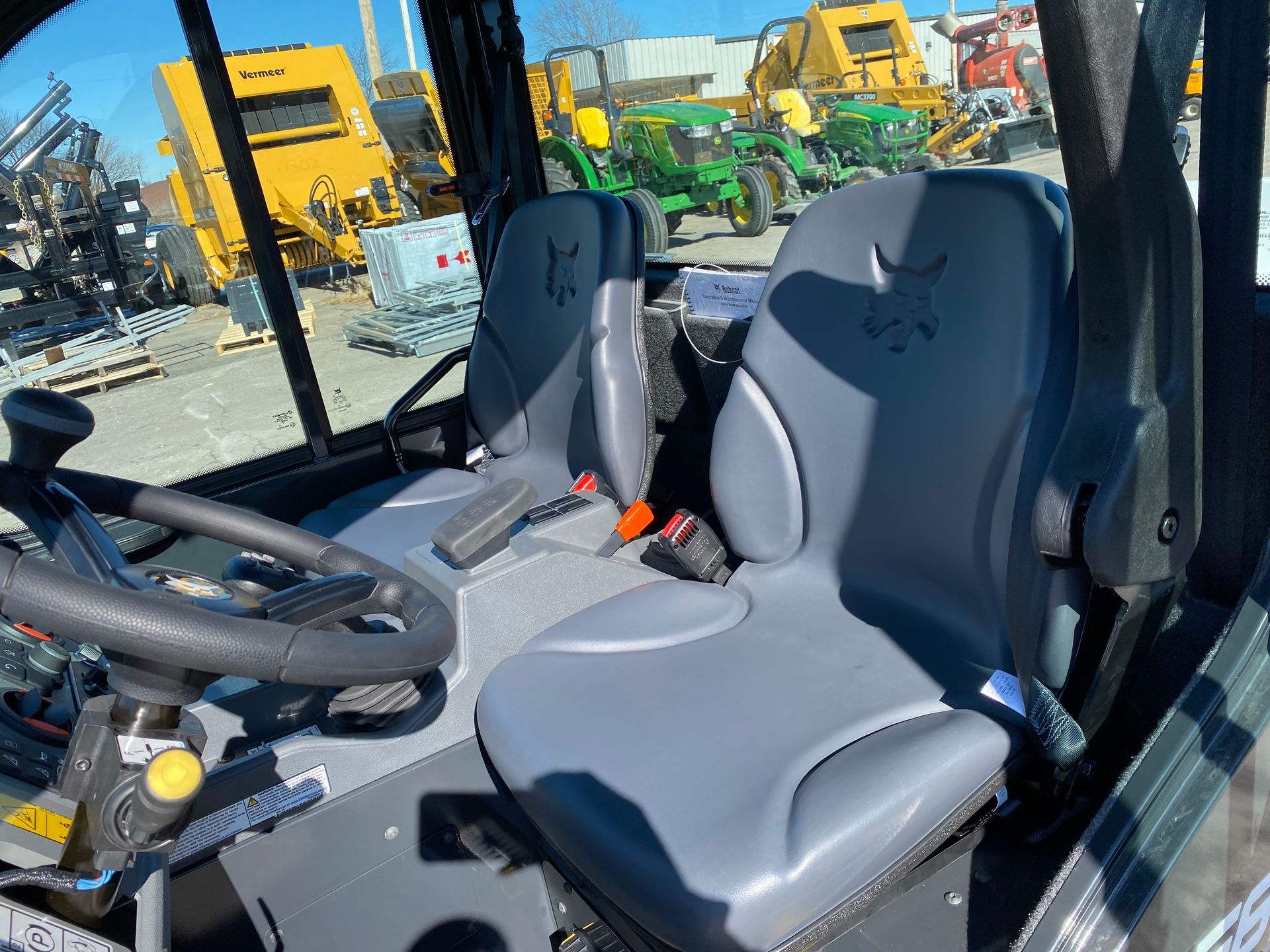 Interior of a vehicle cab with two gray seats, steering wheel, and safety belts.