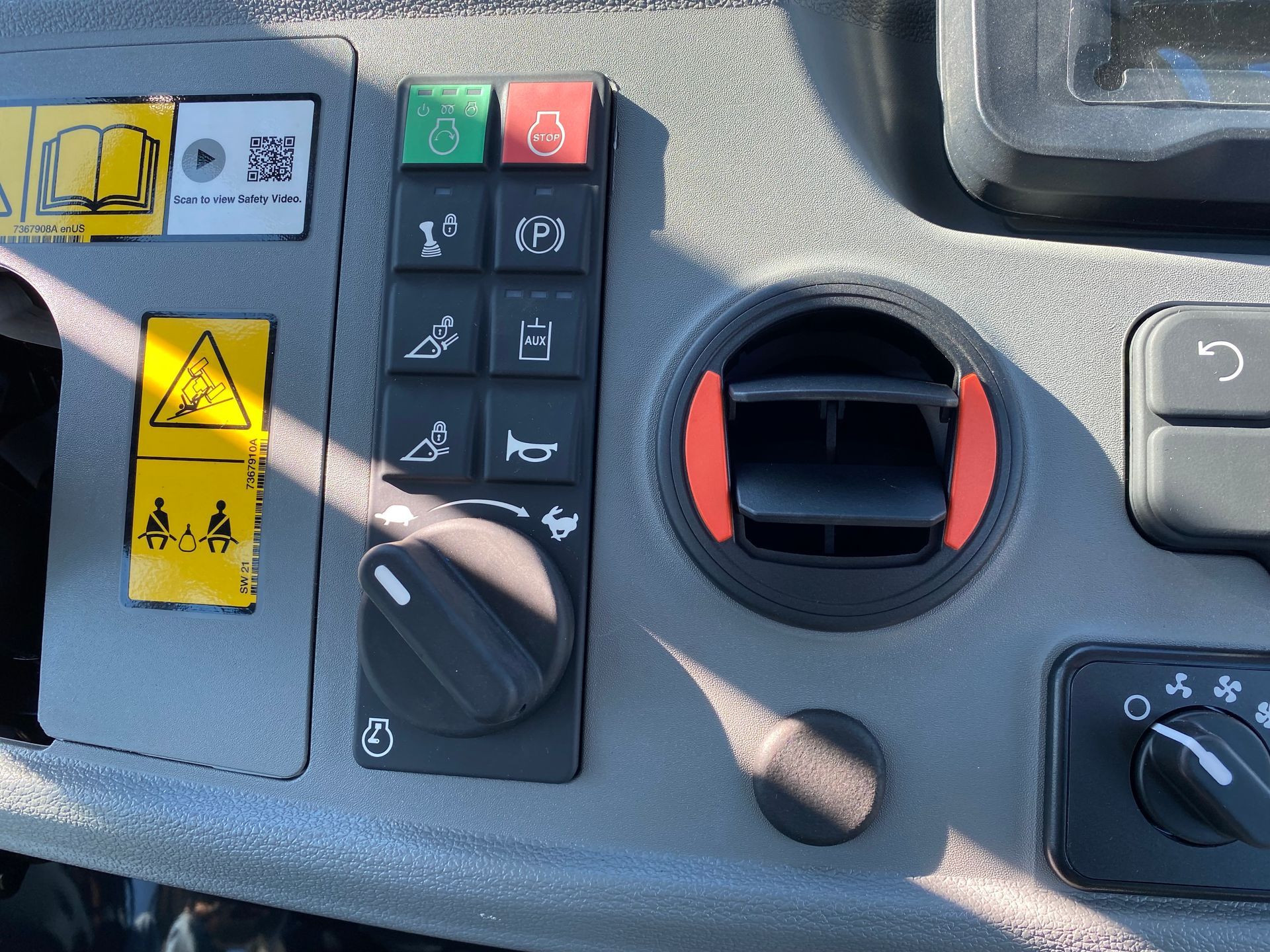 Control panel with buttons, dial, and air vent, likely in a vehicle.