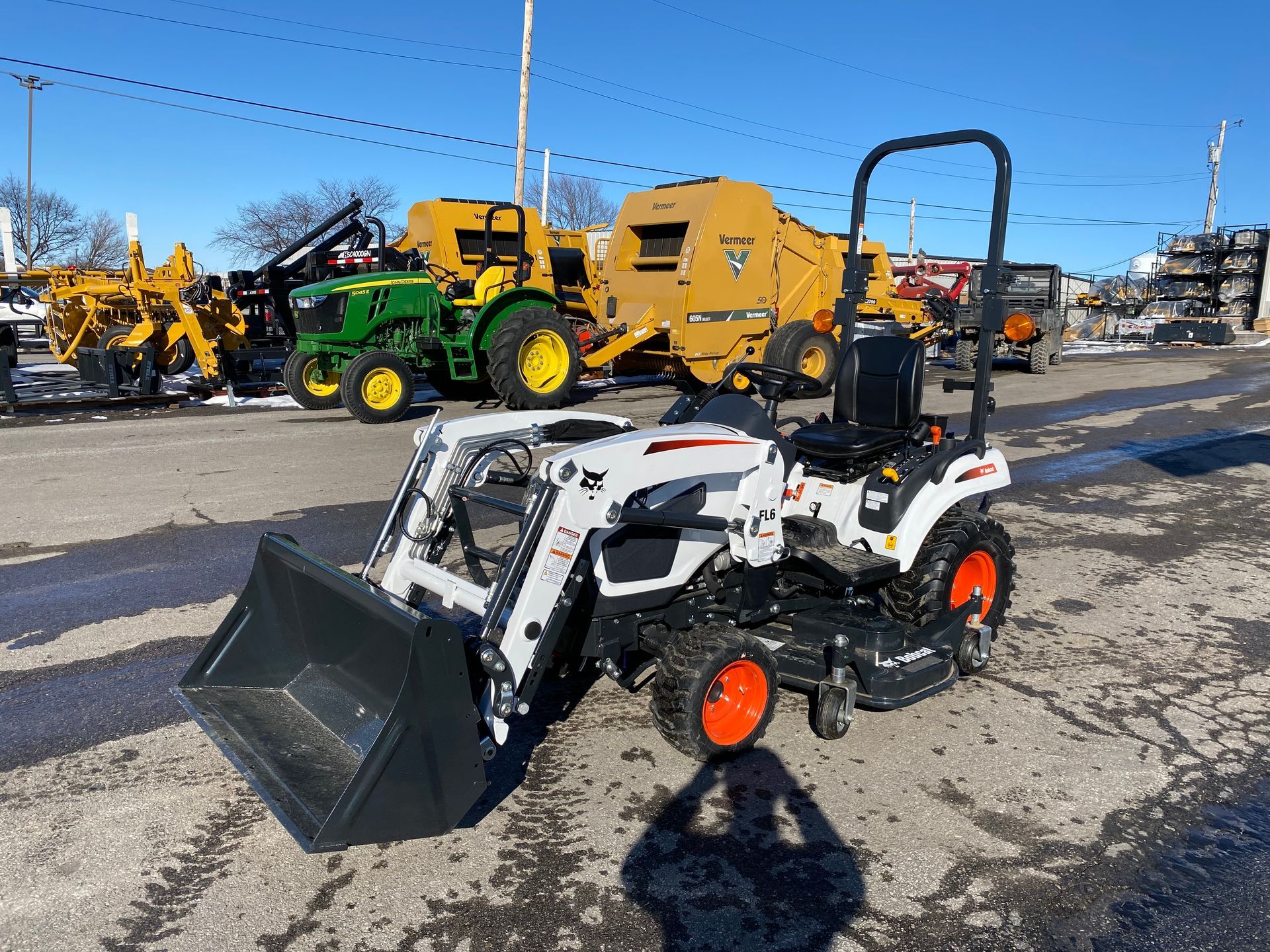White Bobcat tractor with loader bucket, parked outside, other farm equipment in the background.