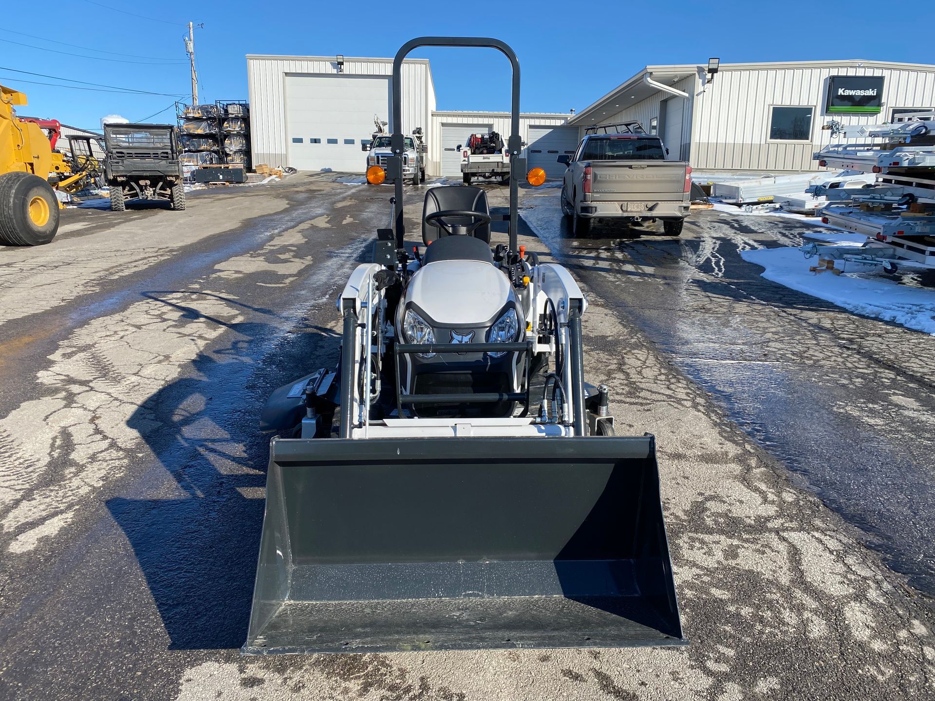 White tractor with front loader on an asphalt surface, in front of buildings, on a sunny day.