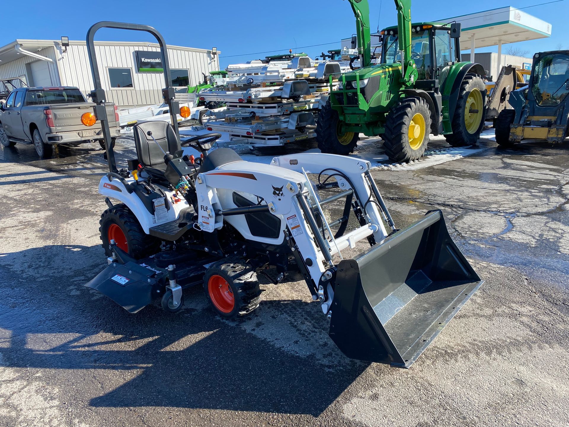 White Bobcat tractor with loader and a tiller on a snowy lot.
