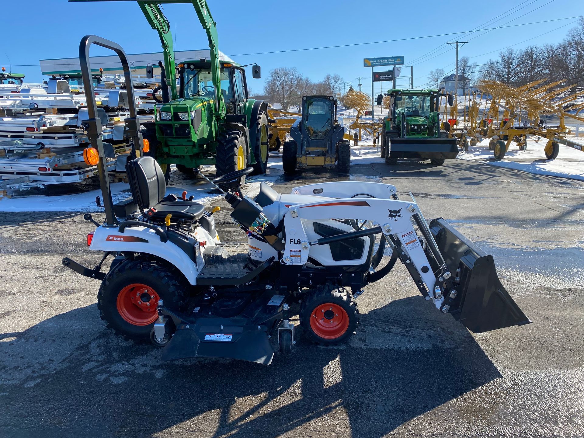 White Bobcat tractor with loader in a lot with other tractors. Sunny day, snow on ground.