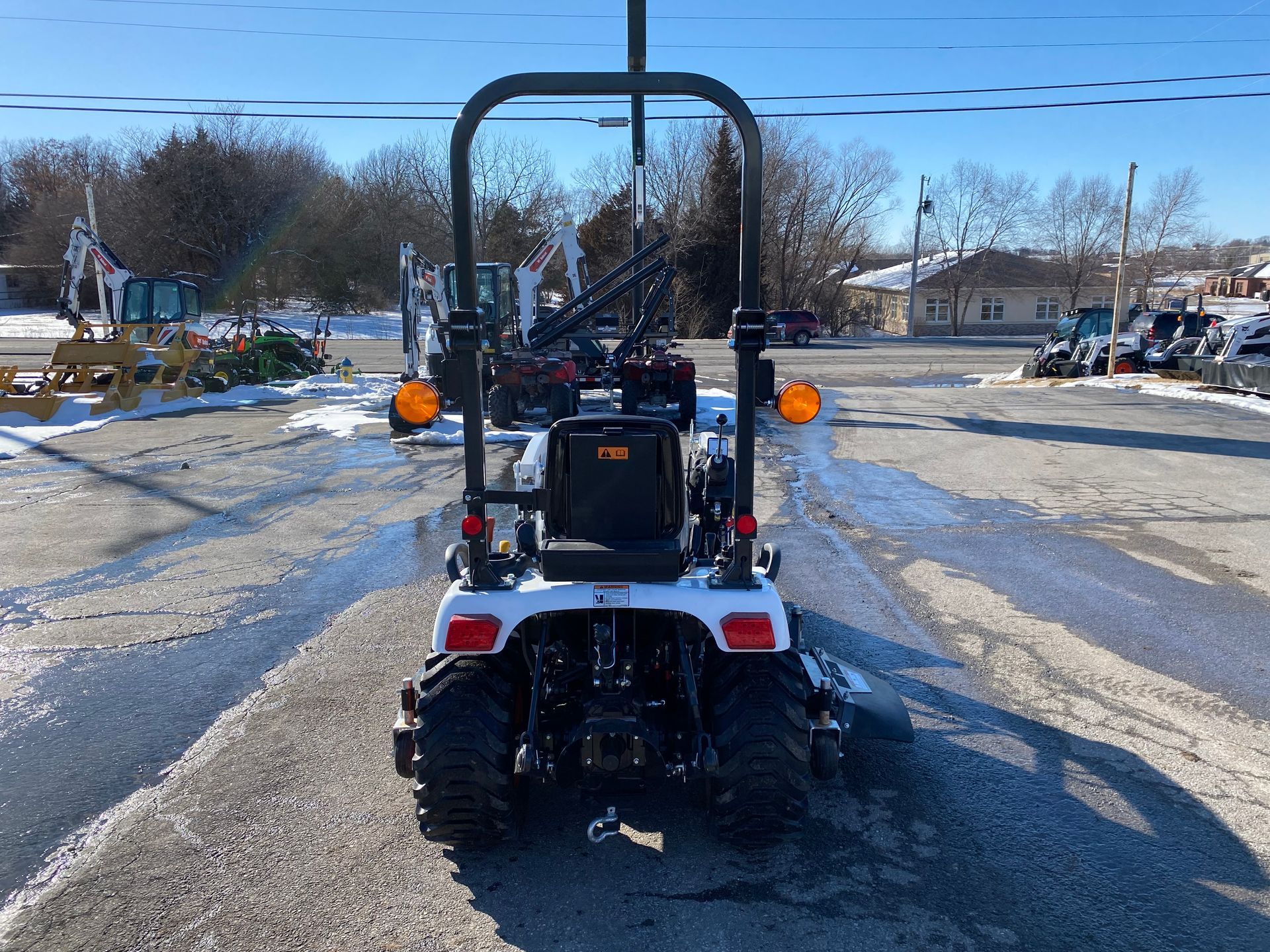 White tractor from rear with roll bar, orange lights, and snow-covered ground.