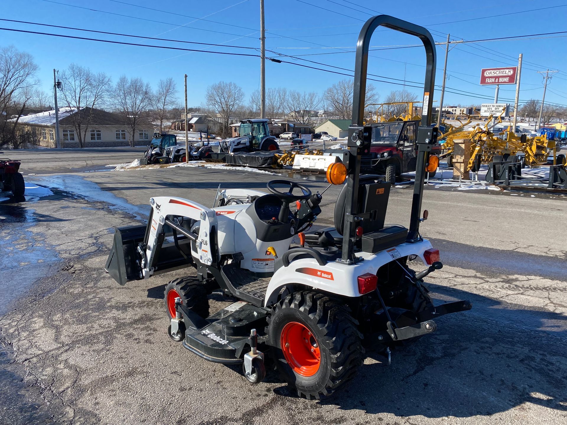 White and orange Bobcat tractor with a front loader and backhoe in a snowy outdoor lot.