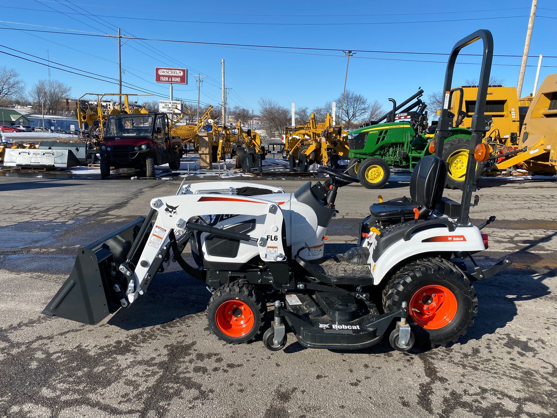 White Bobcat tractor with a front loader and orange wheels, parked outdoors on asphalt.