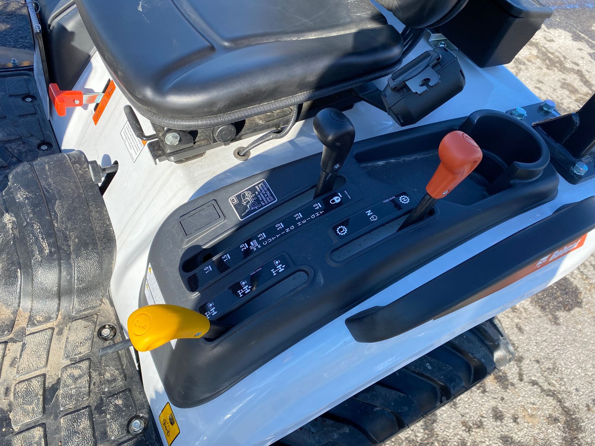 Close-up of tractor controls: black seat, levers with yellow and orange handles, gauges on a white console.