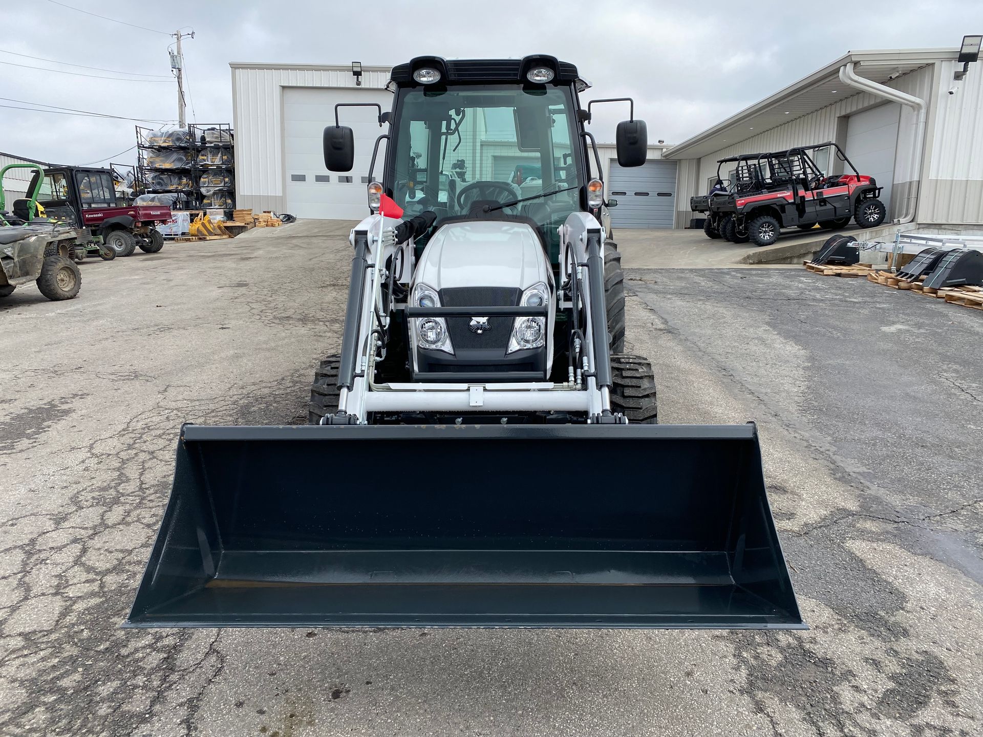 Front view of a white tractor with a black bucket, parked outside a building.
