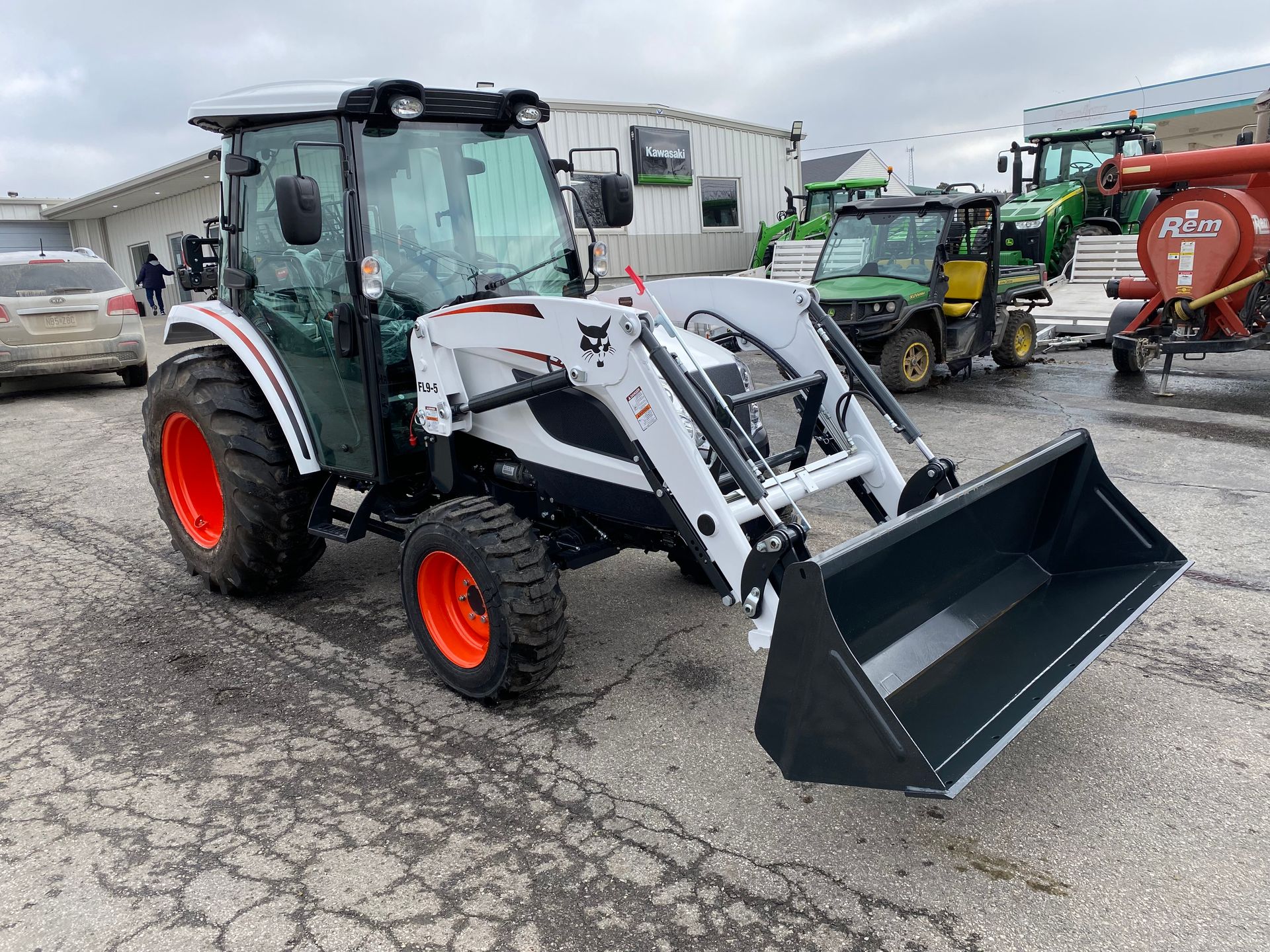 White and gray Bobcat tractor with orange wheels and a front loader, parked outside.