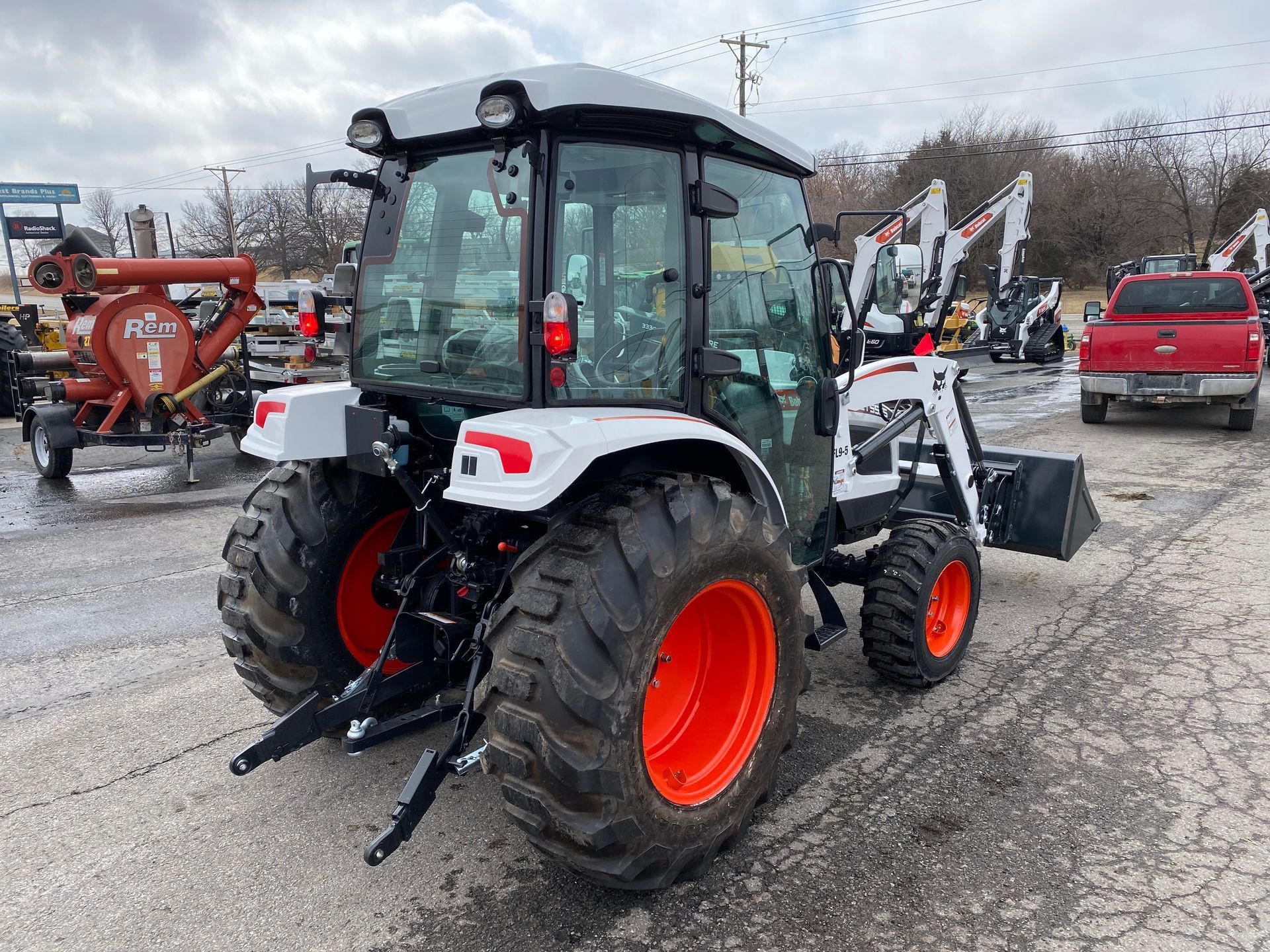Bobcat tractor with a cab, orange wheels, and a front-end loader parked outside on a cloudy day.