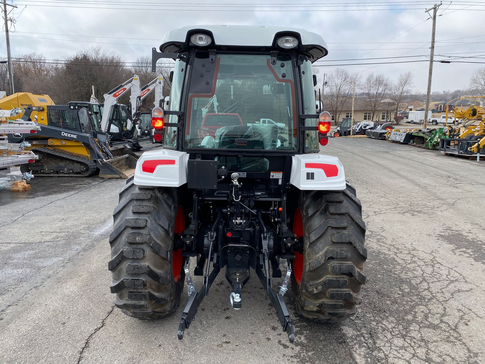 Rear view of a white and gray tractor with large tires, parked on a cracked asphalt lot.