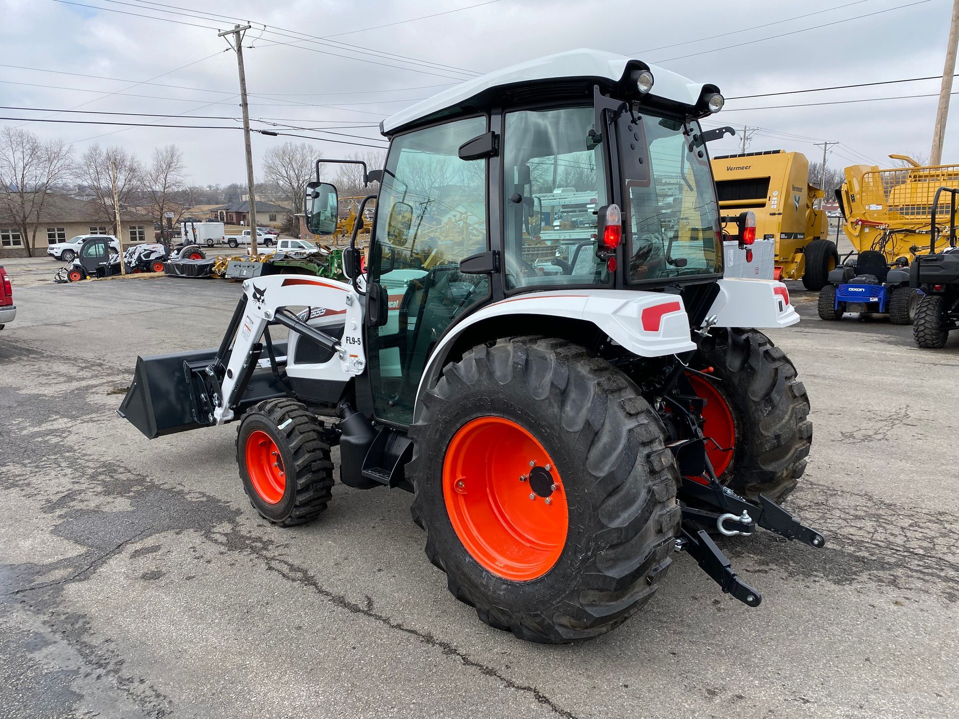 White and orange Bobcat tractor with cab, parked outdoors.