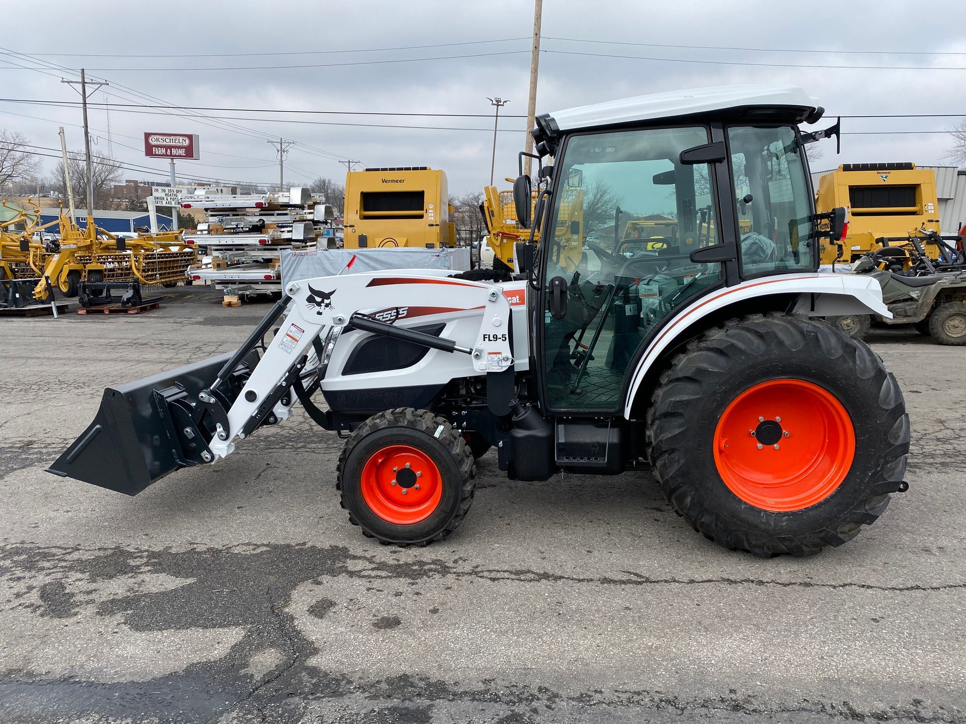 Bobcat tractor with a front-end loader on an asphalt lot. White cab, black bucket, orange wheels.