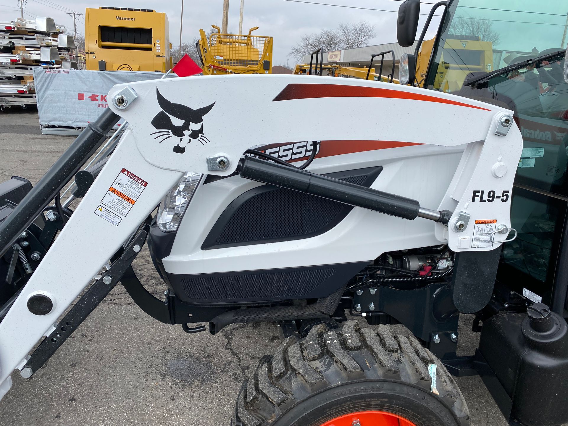 White Bobcat tractor with loader arm, black grill, orange and white accents, parked outside.